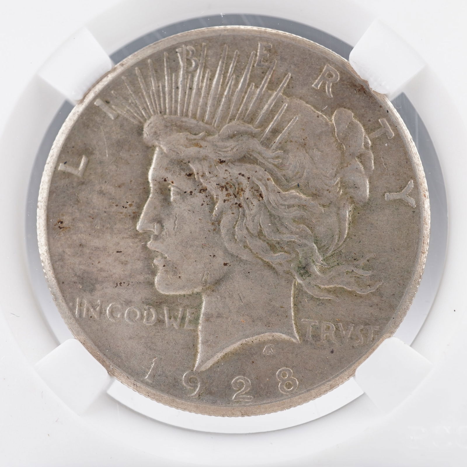 1928 United States Silver Peace Dollar Coin: The obverse features the image of Liberty wearing a radiant crown, with the inscriptions LIBERTY, IN GOD WE TRVST, and the date 1928. The reverse shows an eagle perched on a rock clutching an olive