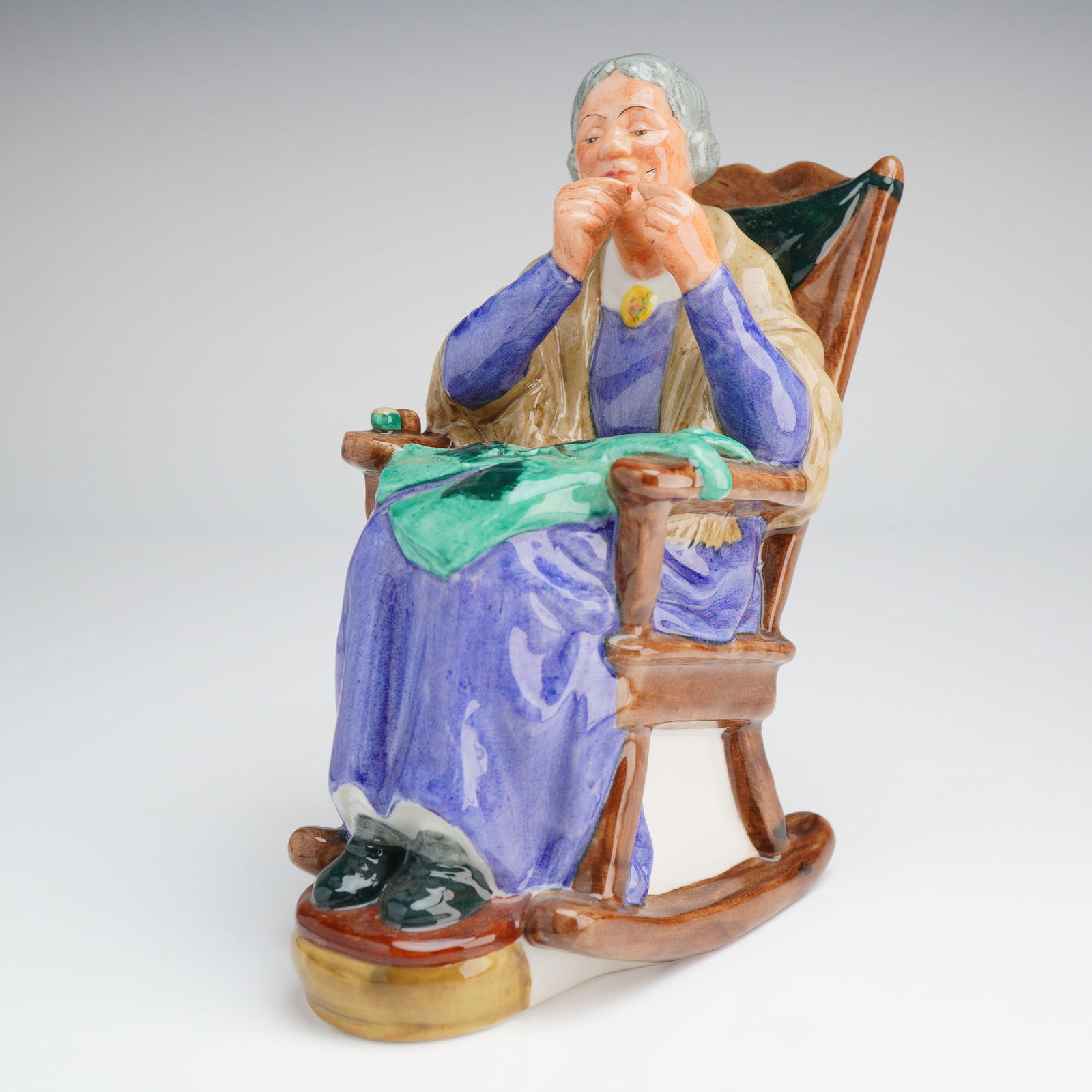 Royal Doulton Figurine A Stitch in Time HN2352: This Royal Doulton Porcelain Figurine, A stitch in time (HN2352), depicts an elderly woman dressed in purple and tan sitting in a brown rocking chair, bearing the 1965 copyright mark. Dimensions: 3.00