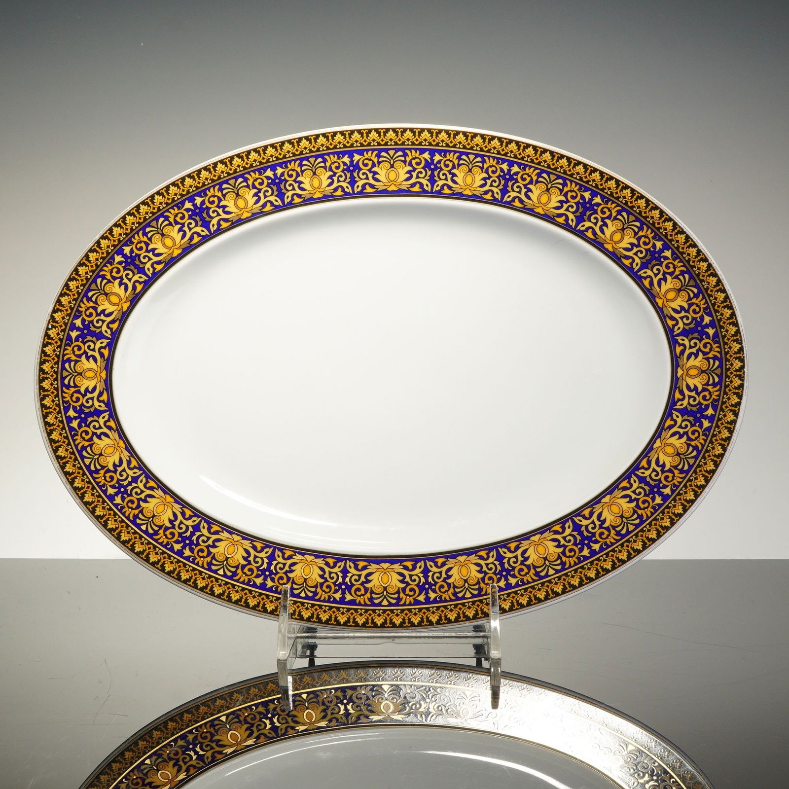 Rosenthal Versace Porcelain Oval Serving Platter, Medusa Blue: The dish features a wide border with an intricate gold-toned neoclassical scroll and floral pattern set against a vibrant cobalt blue ground, surrounding a plain white glazed center. The reverse is ma