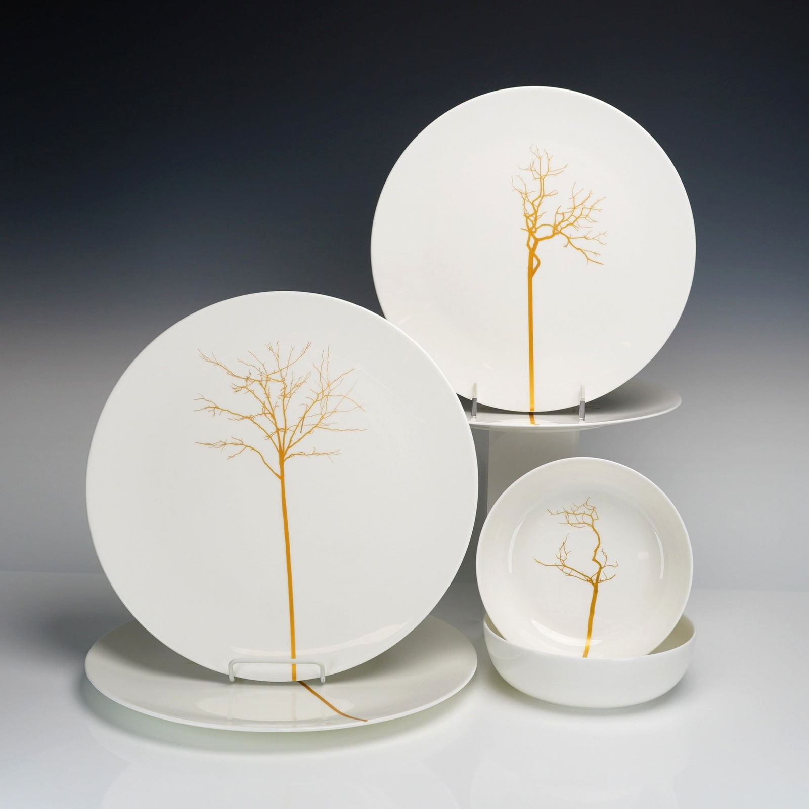 6pc Dibbern Germany Porcelain Plates, Bowls & Chargers, Golden Forest: A 6pc collection designed by Bodo Sperlein. The collection includes two 7" bowls, two 12" chargers, and two 10" dinner plates. Each piece is crafted from white glazed porcelain and decorated with a mu