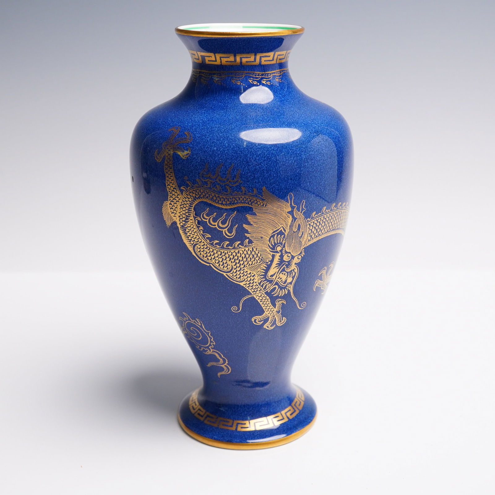 Wedgwood Fairyland Vase, Celestial Dragon Z4616: This footed vase features a powdered blue exterior ground with gilt decorations throughout. The central motif on one side displays a 'Celestial Dragon', depicted in intricate gold with defined scales,