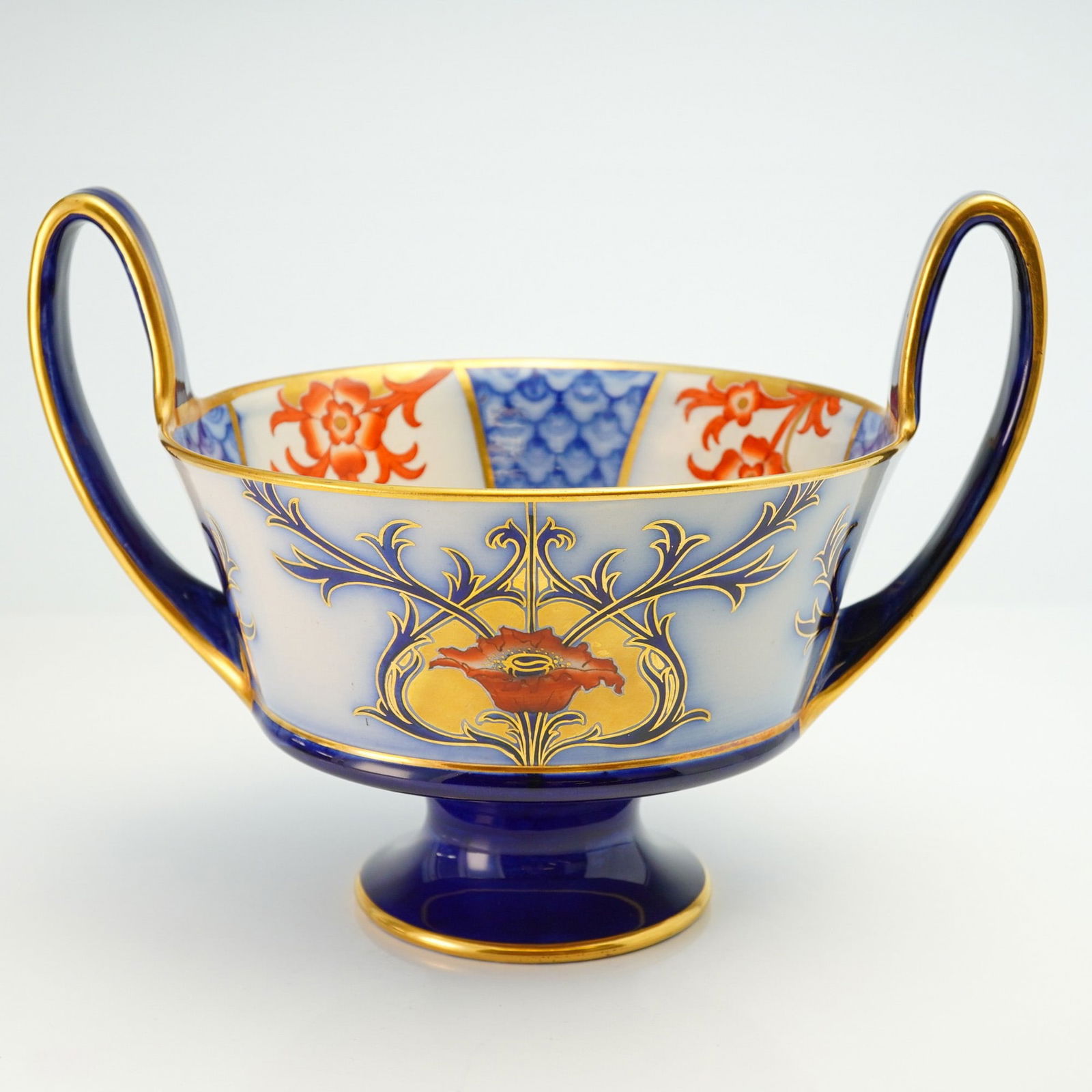 Moorcroft Macintyre Twin Handled Vase, Aurelian Poppy: An English footed bowl with slender handles, showcasing the Aurelian Poppy design. The surface is richly embellished with gilt accents, vibrant blue and red flowers, and scrolling foliage, along with