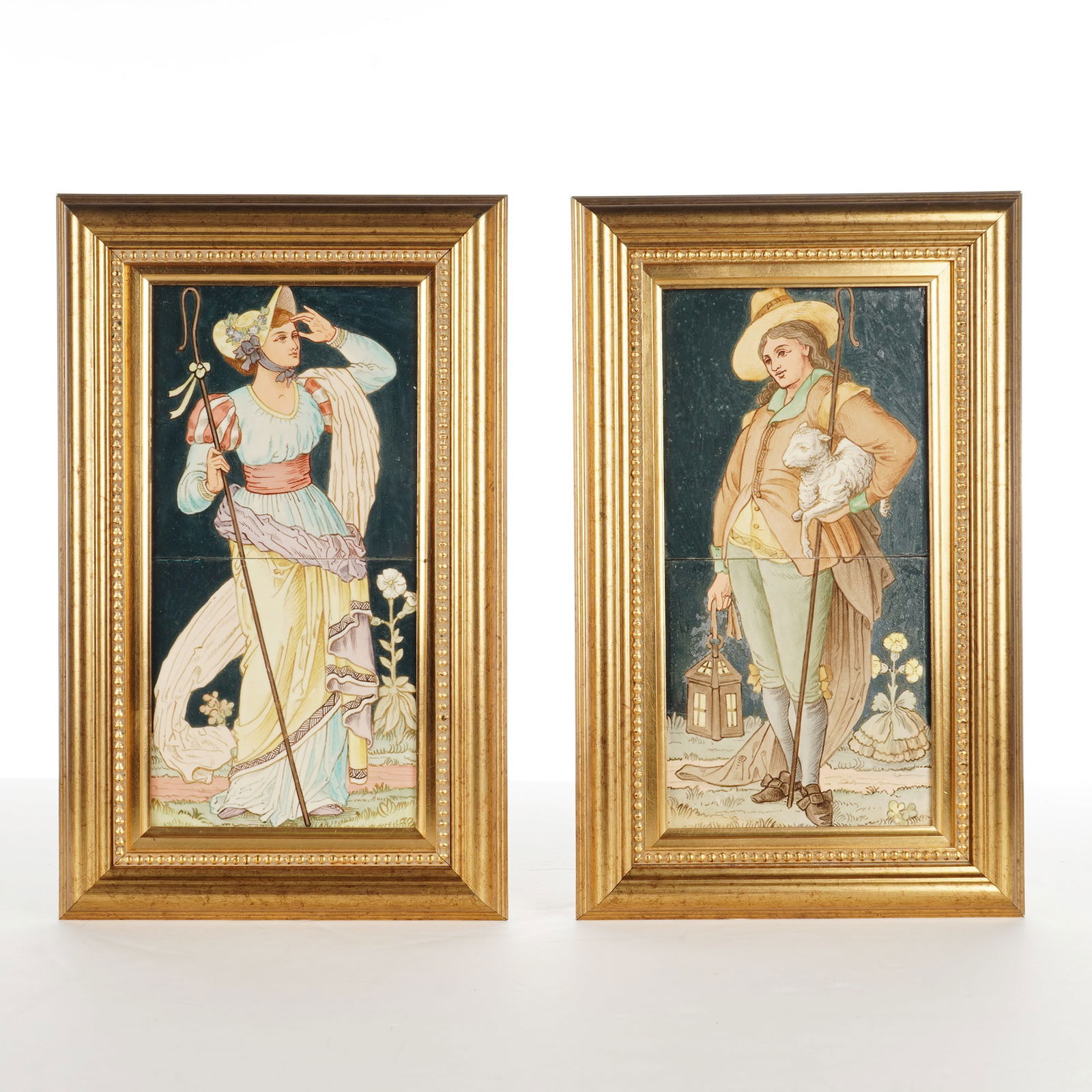 Pair of Framed Ceramic Shepherd and Shepherdess Tile Plaques: A set of two-tile panels depicting a shepherd and shepherdess against a dark blue ground. The shepherd holds a white lamb and crook in one hand and a lantern in the other, rendered in shades of