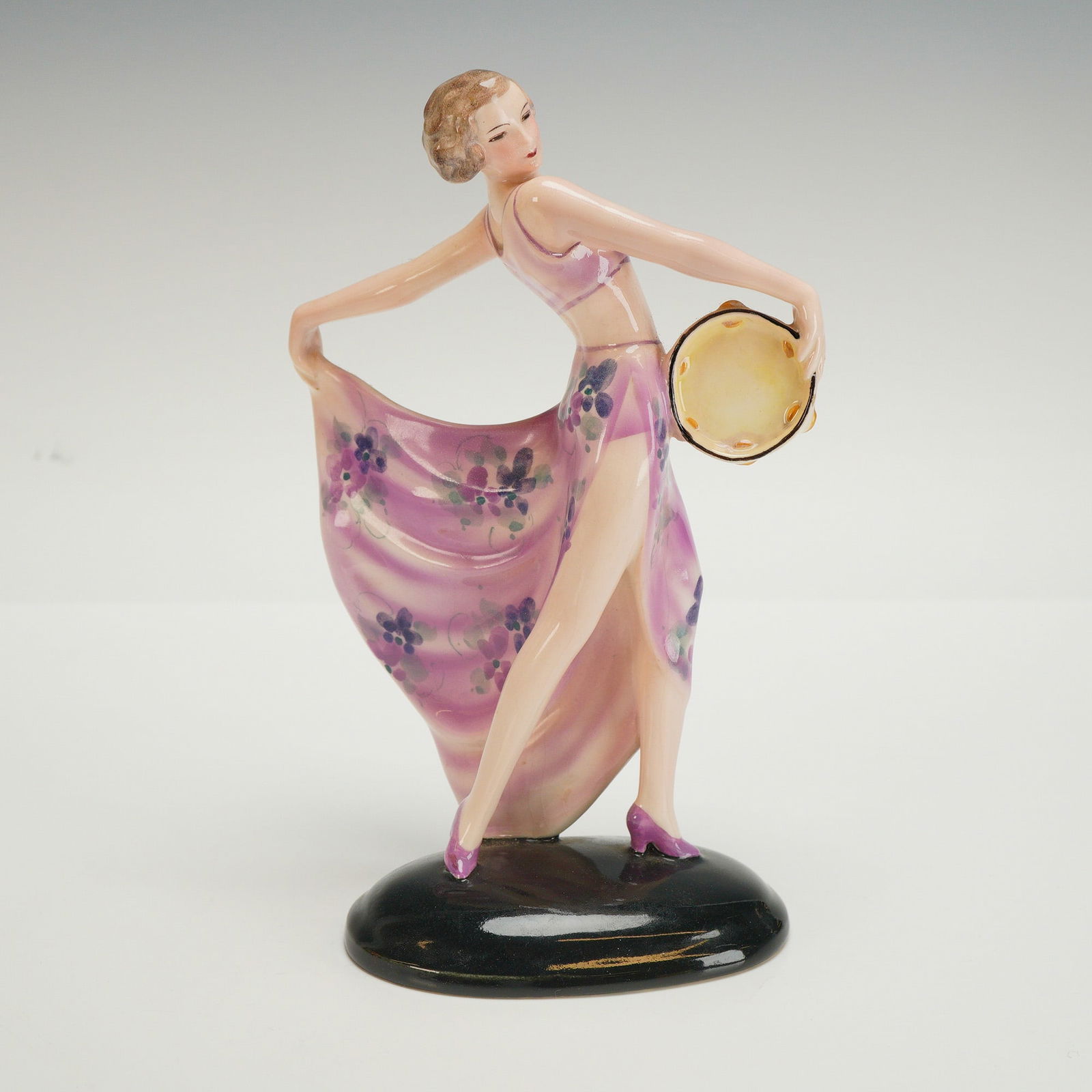Goldscheider Josef Lorenzl Figurine, Tambourine Dancer: A figure modeled as a woman in a pink floral outfit, with one hand holding her skirt, and the other hand holding a tambourine. Signed Lorenzl to the base, impressed with model number 6759, additional