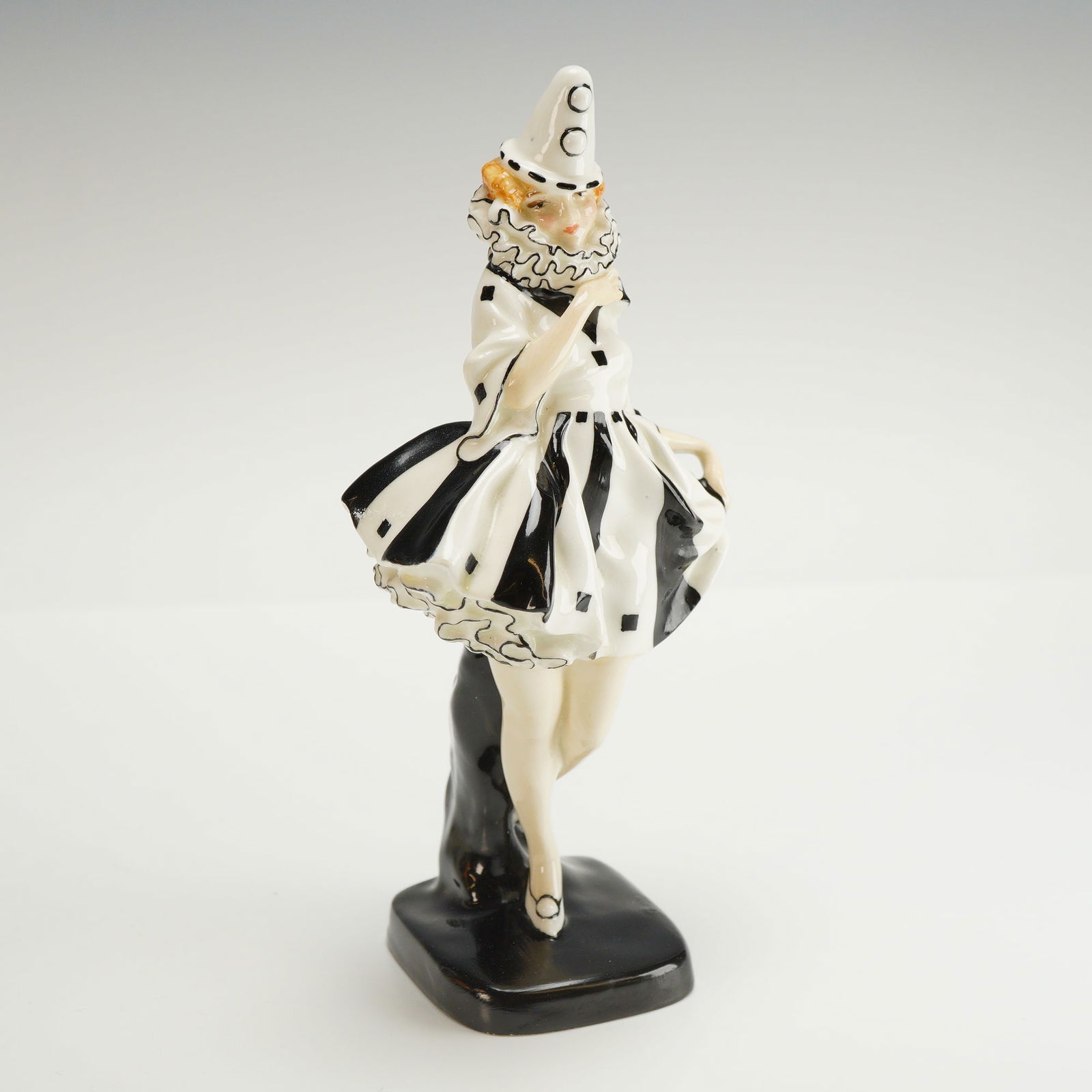 Royal Doulton Figurine, Pierrette HN721: A glazed hand decorated figure modeled as a female theatrical clown. She is posed mid-step in a flared black and white costume with a striped pattern on the skirt. The base is marked with the Royal