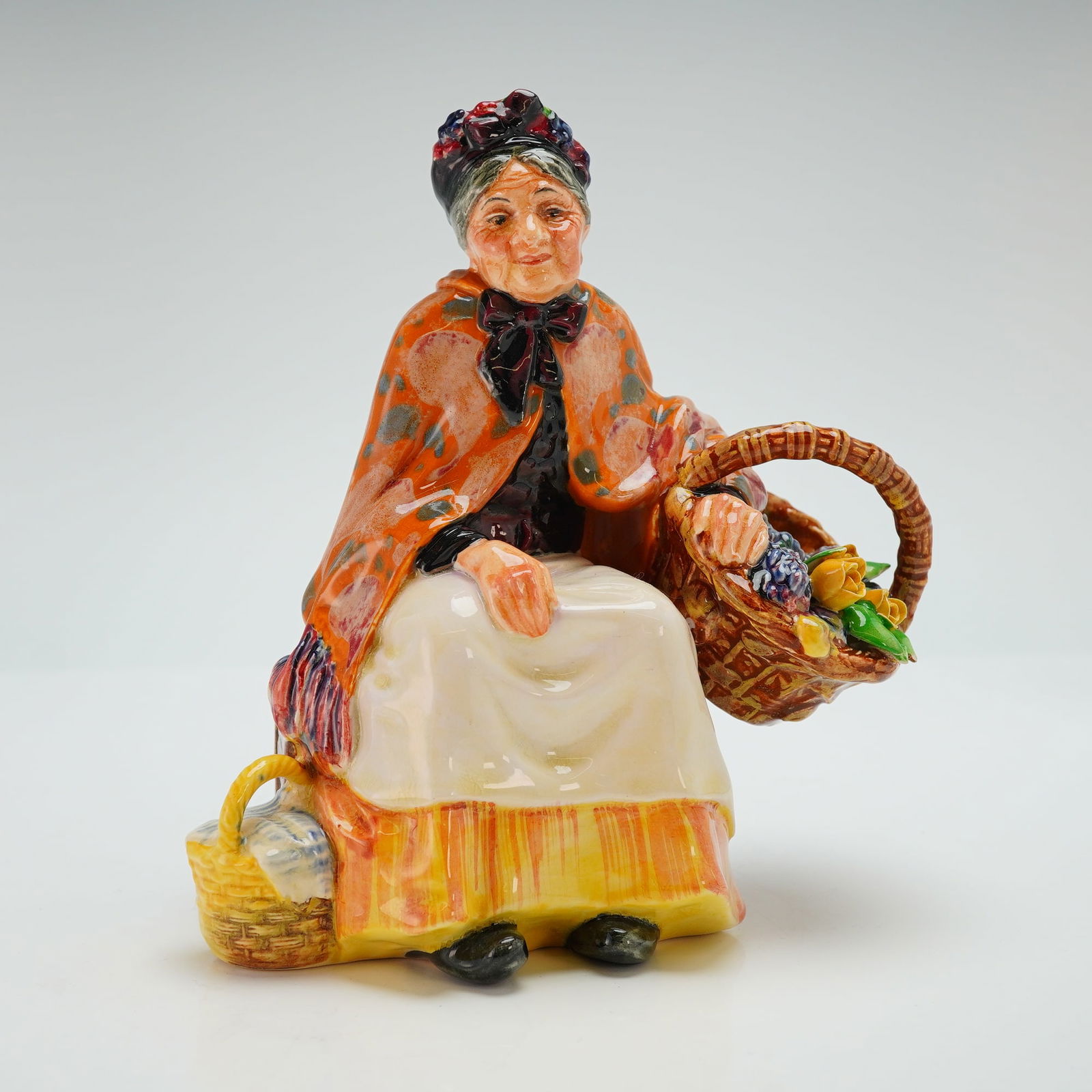 Royal Doulton Figurine, Old Lavender Seller HN1571: Designed by Leslie Harradine as part of the Street Vendor series. The piece portrays an elderly woman seated with a basket of colorful lavender sprigs in one hand and a second basket by her side, wear