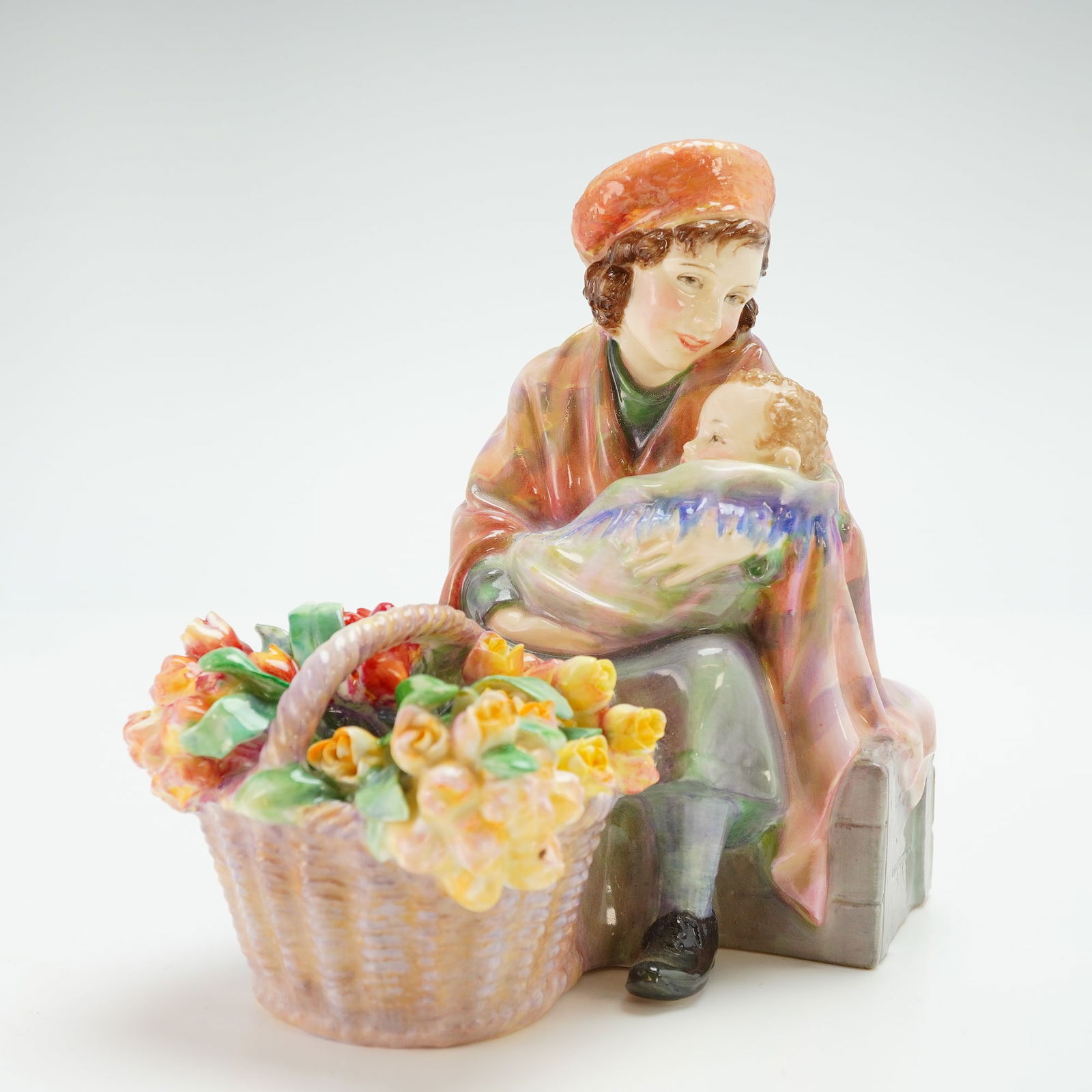 Royal Doulton Rare Colorway Figurine, Curly Knob: A porcelain figurine depicting a young woman seated holding a baby, with a large basket of flowers beside her. She is dressed in a green and purple dress with a pink shawl. Royal Doulton backstamp. Ar