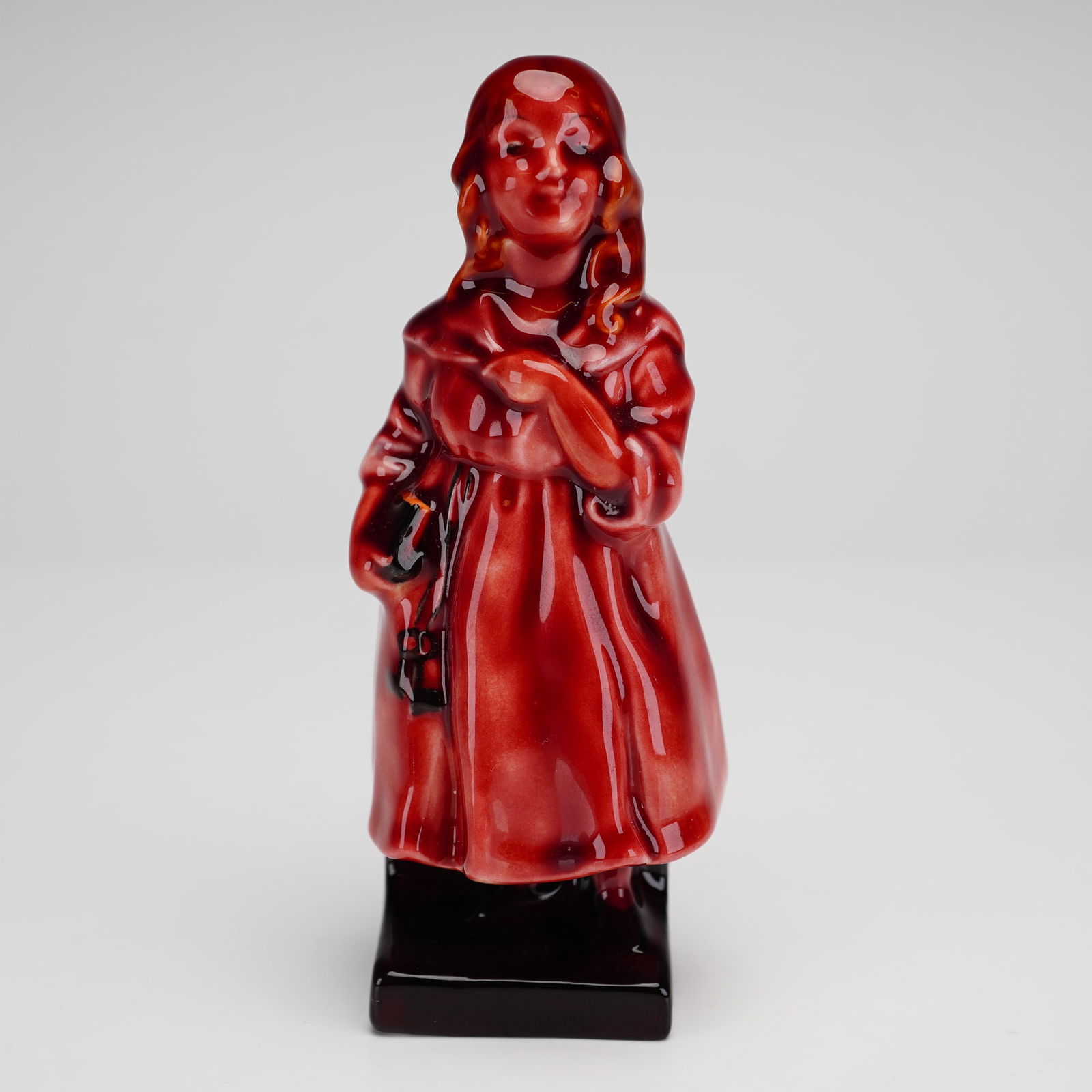 Royal Doulton Flambe Bone China Figurine, Little Nell: Depicting the character Little Nell from Charles Dickens' The Old Curiosity Shop. The object is constructed from bone China and features a red flambe glaze with characteristic tonal variations. The fi