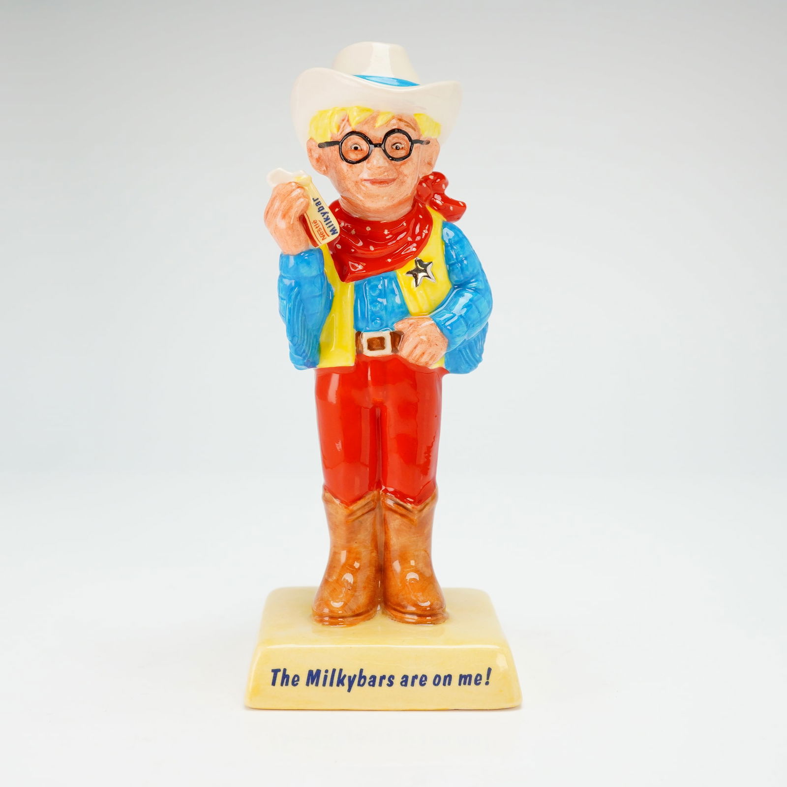 Royal Doulton Advertising Figurine, The Milkybar Kid AC7: A limited edition example depicting a blonde-haired boy wearing spectacles and dressed as a western sheriff, with red pants, a blue shirt, and a yellow vest fitted with a silvery sheriff badge, along