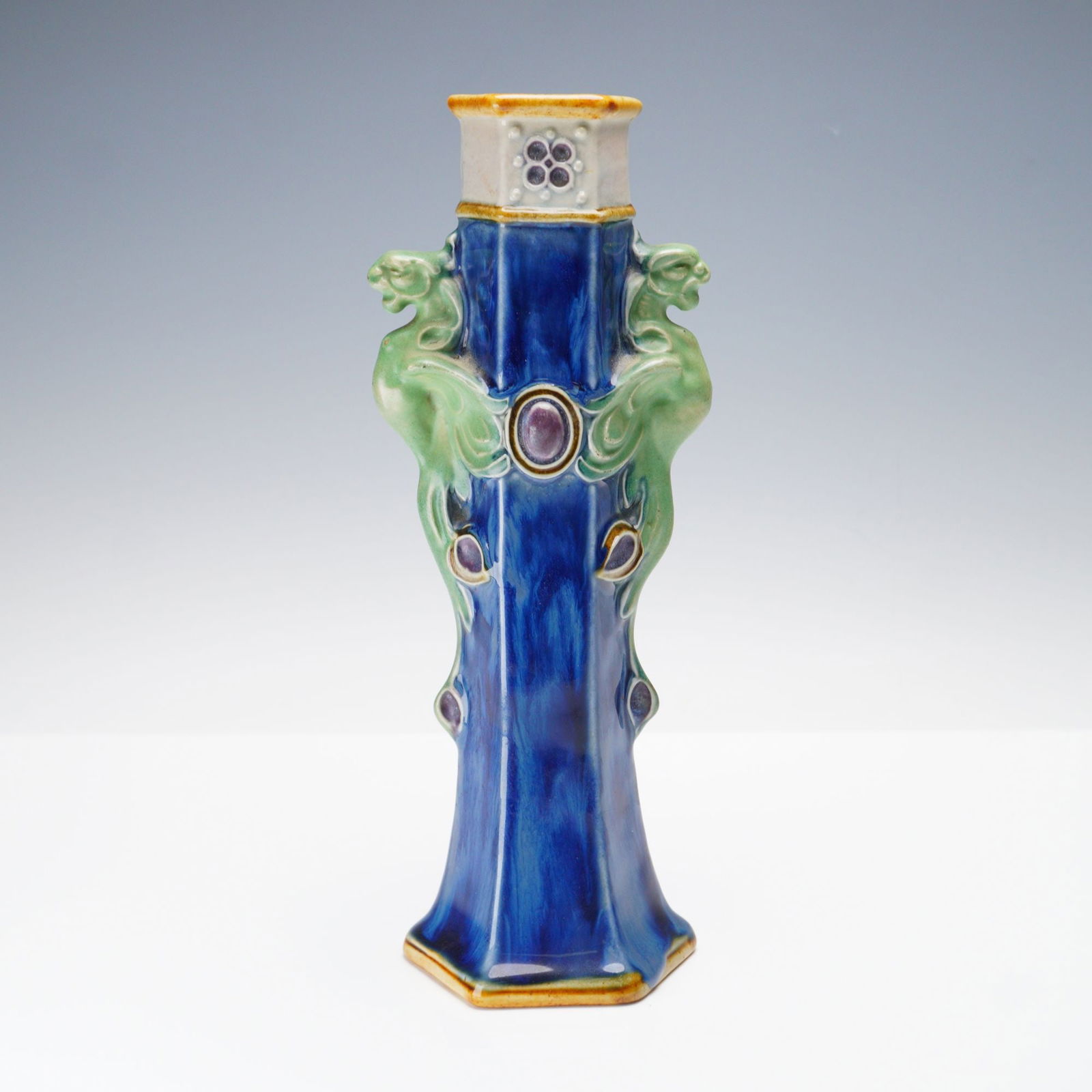 Doulton Lambeth by Francis C. Pope Stoneware Hexagonal Sleeve Vase: A hexagonal stoneware sleeve vase of elongated tapering form. Features relief applied grotesque gargoyle handles on either side in a green hue. Finished in a dramatic cobalt blue tone. F. C. P. incise