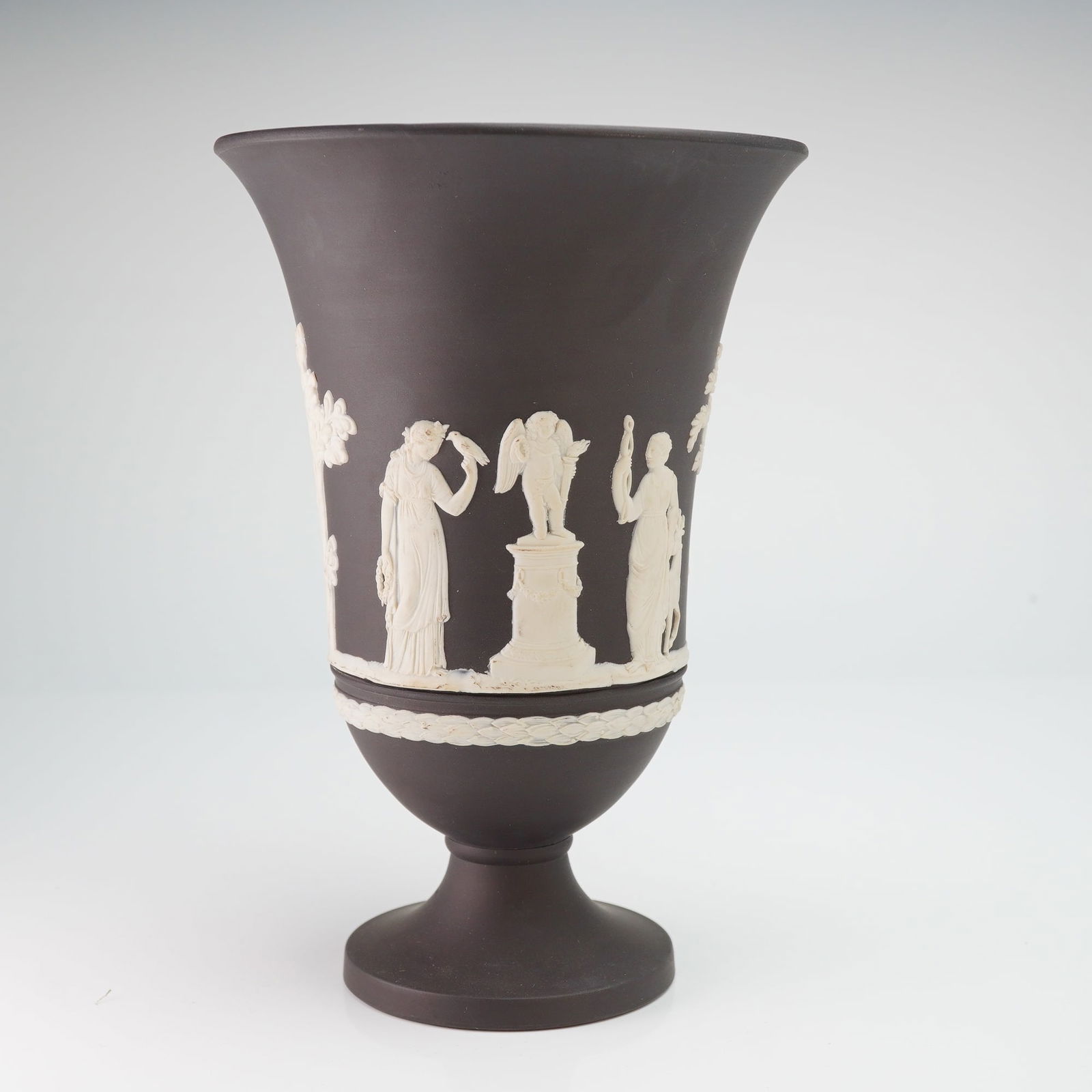 Wedgwood Black Basalt Neoclassical Vase: This Wedgwood black jasperware urn shaped vase is composed of a matte black stoneware body featuring white bas-relief decoration in the Neoclassical style. The central frieze depicts classical figures