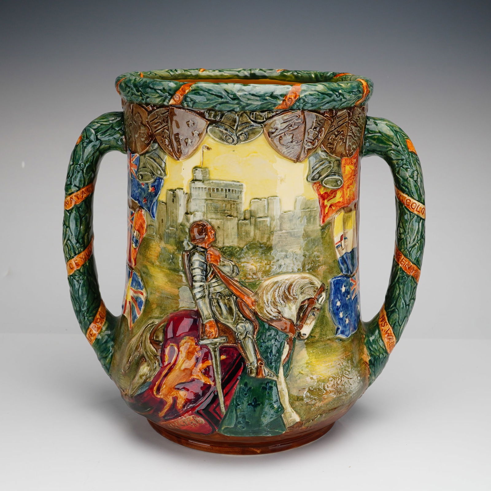 Royal Doulton Silver Jubilee Loving Cup, King George V and Queen Mary: A Royal Doulton ceramic loving cup produced to commemorate the 1935 Silver Jubilee of King George V and Queen Mary. The vessel features high-relief molded decoration with a polychrome glaze. One side