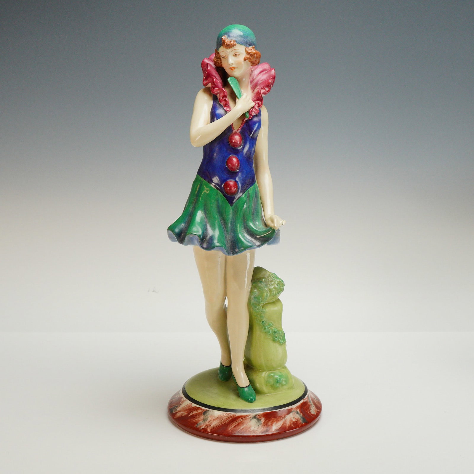 Royal Dux Bohemia Porcelain Art Deco Lady Figurine: A hand painted figure depicting a woman in a blue and green dress with a pink ruffled collar, holding a fan near her chest. The base features the Royal Dux pink triangle mark and is impressed with 300