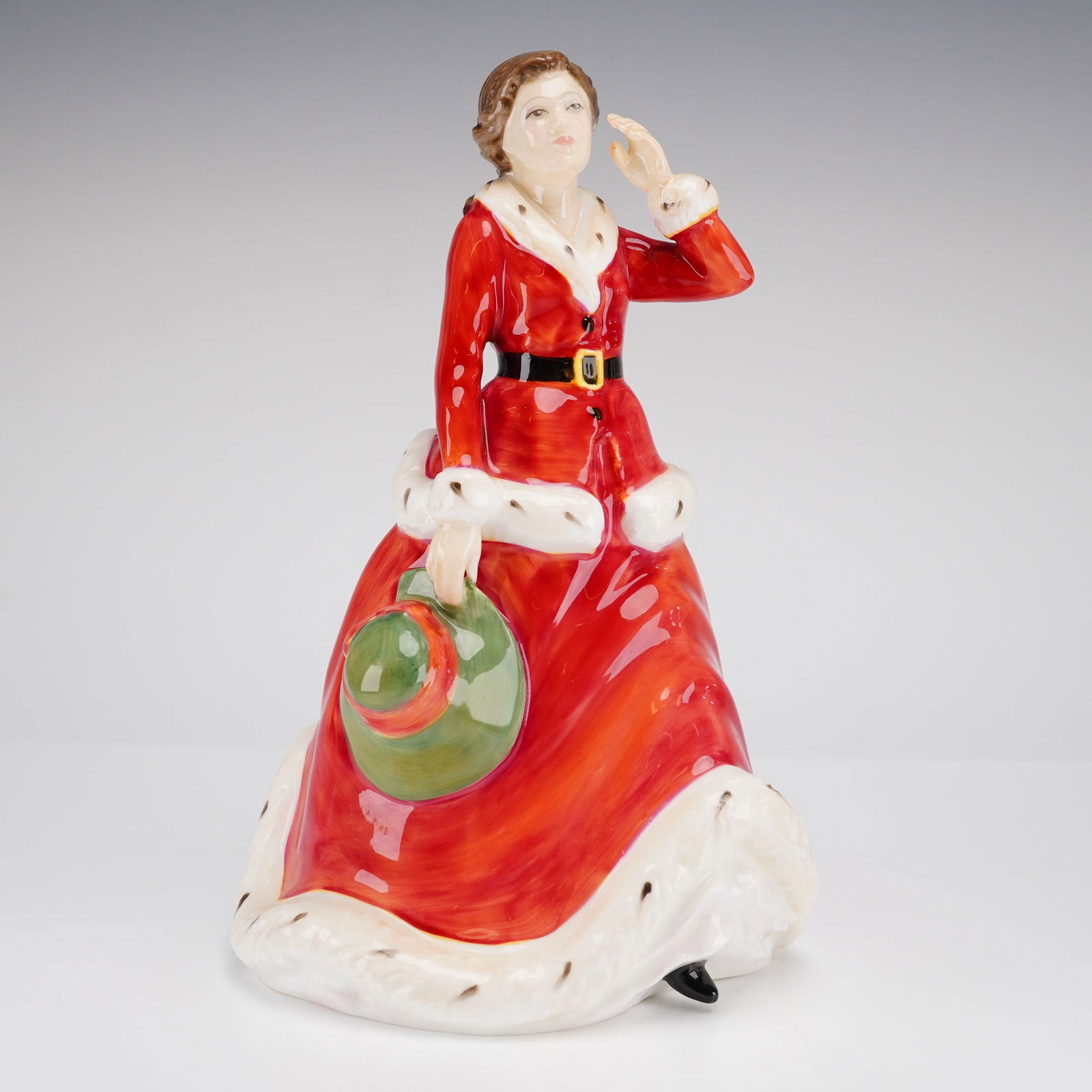 Royal Doulton Figurine Winter's Day HN3769: A glazed bone china figurine by Royal Doulton, modelled by Nada M. Pedley. The figurine depicts a woman in a red, fur-trimmed outfit holding a green hat. The underside features the Royal Doulton backs