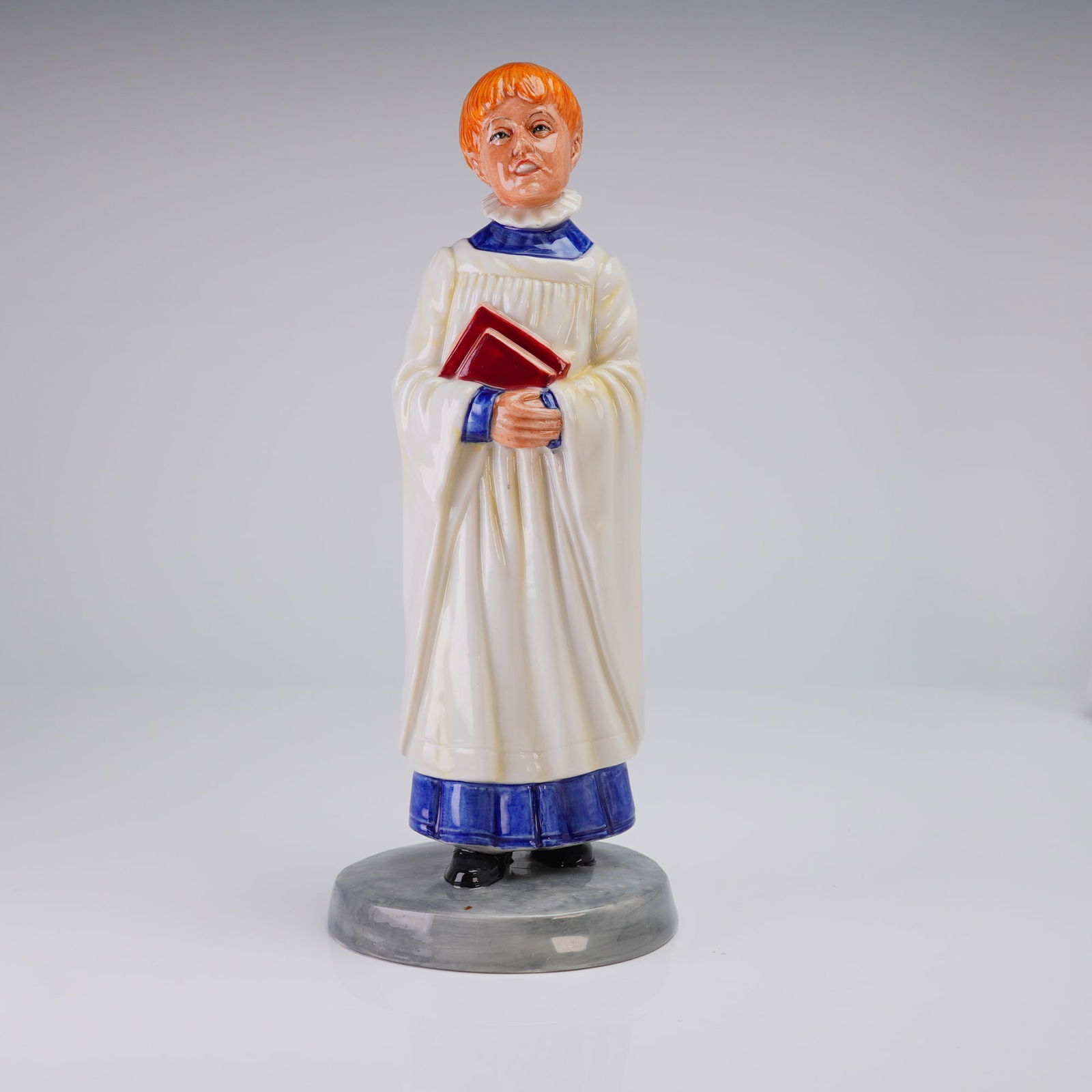 Royal Doulton Prototype Factory Proof Figurine, Choir Boy: An English porcelain figurine with glazed finish depicting a choir boy holding two books, dressed in a white surplice over a blue cassock. The underside is marked with the Royal Doulton backstamp. "Fa