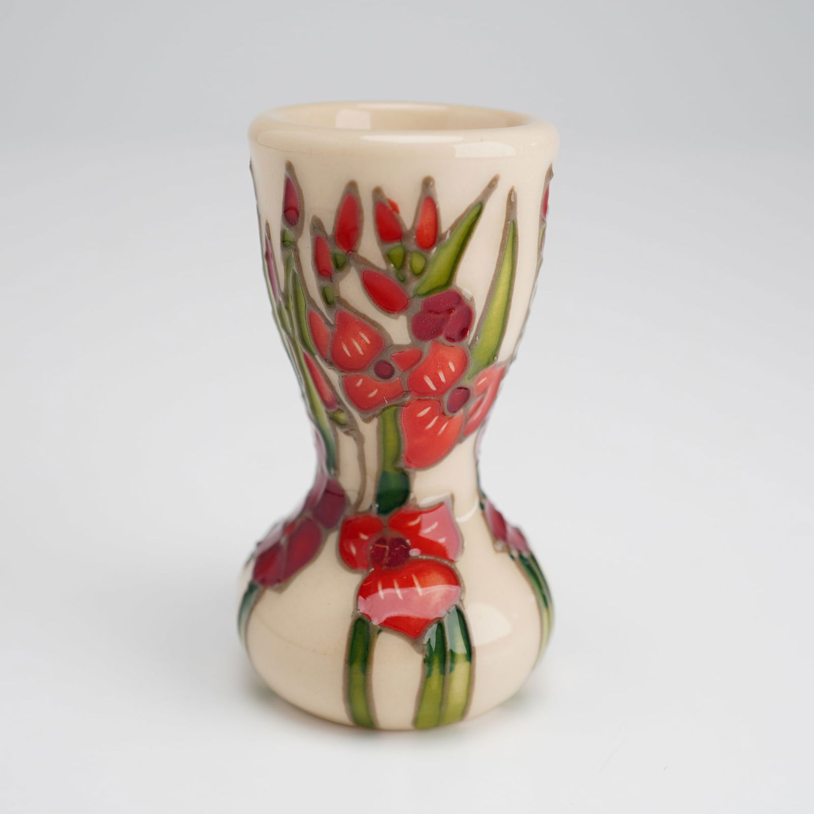 Moorcroft Miniature Floral Months of The Year Vase, Gladiolus: This Moorcroft tiny vase is a Moorcroft Miniature Floral Months of The Year Vase featuring a Gladiolus design. The waisted ceramic form represents the month of August. The decoration depicts red and p
