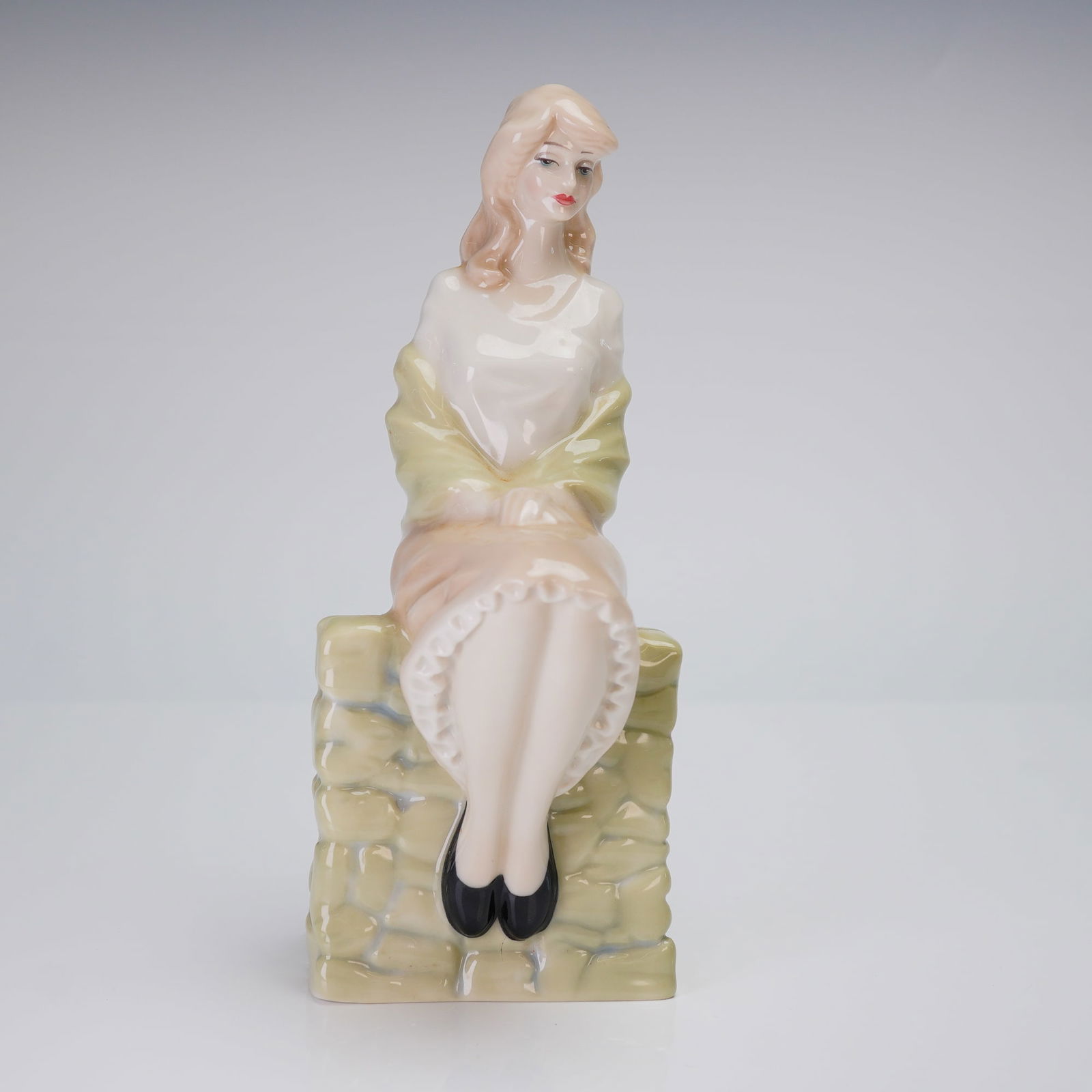 Royal Doulton Figurine, Reflections Entranced HN 3186: The figurine depicts a young woman seated on a pale green, stone-like plinth. She is rendered wearing a white blouse, a pink skirt, and a light green shawl. The underside of the base features the Roya