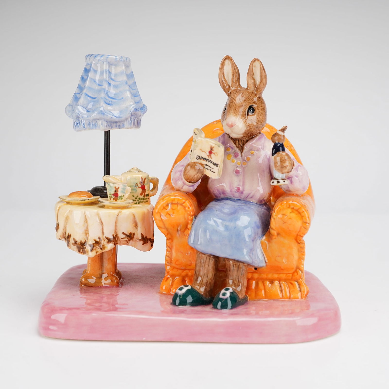 Royal Doulton Limited Edition Bunnykins Mrs. Collector DB335 Figurine: This Royal Doulton limited edition Bunnykins figurine, titled Mrs. Collector (DB335), is a hand-painted ceramic tableau. The piece depicts an anthropomorphic female rabbit seated in an orange armchair