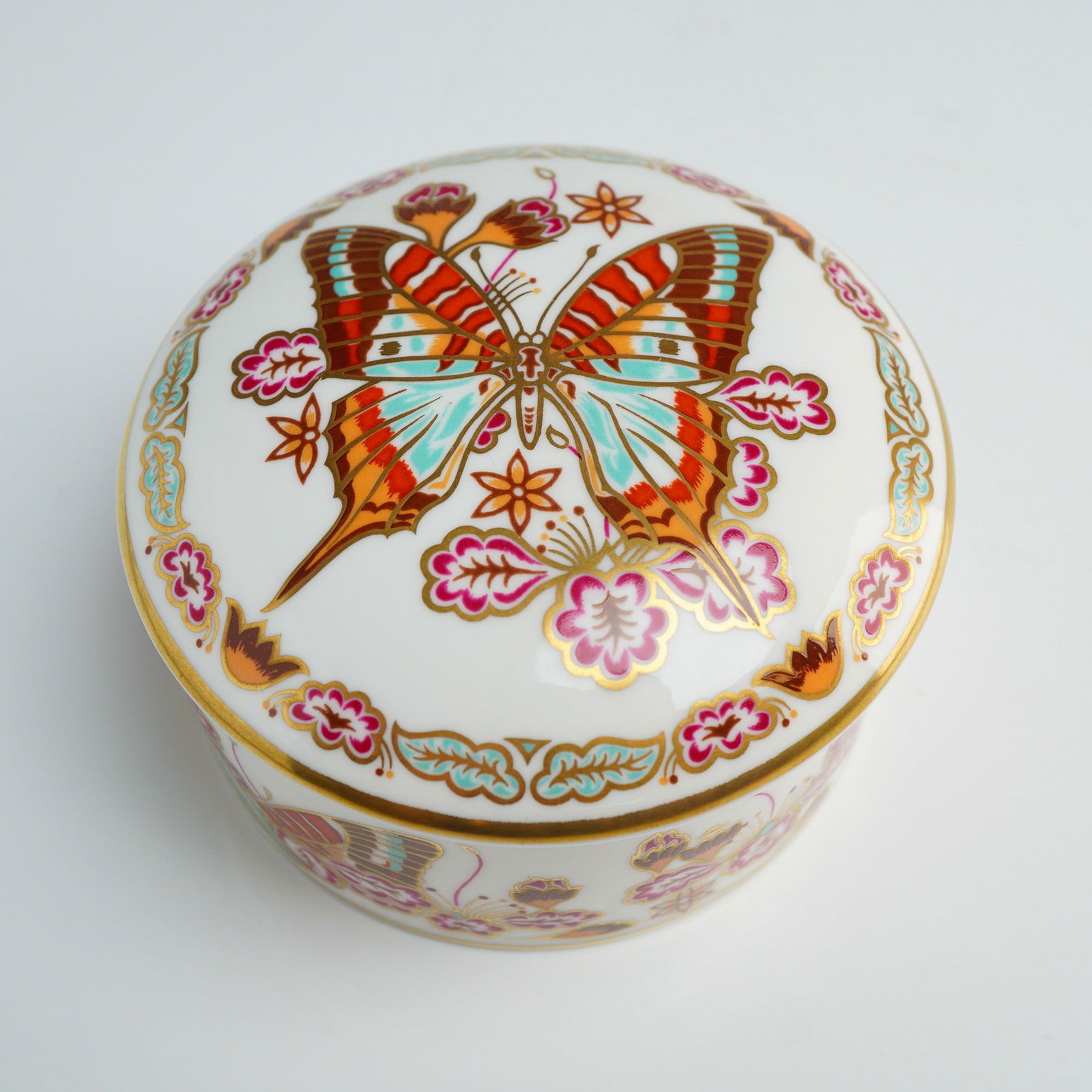 Royal Crown Derby Butterflies of the World Lidded Trinket Box: A Royal Crown Derby English bone china circular lidded trinket box from the Butterflies of the World series, featuring the Eastern Fivebar Swordtail design. The white china body is decorated with butt