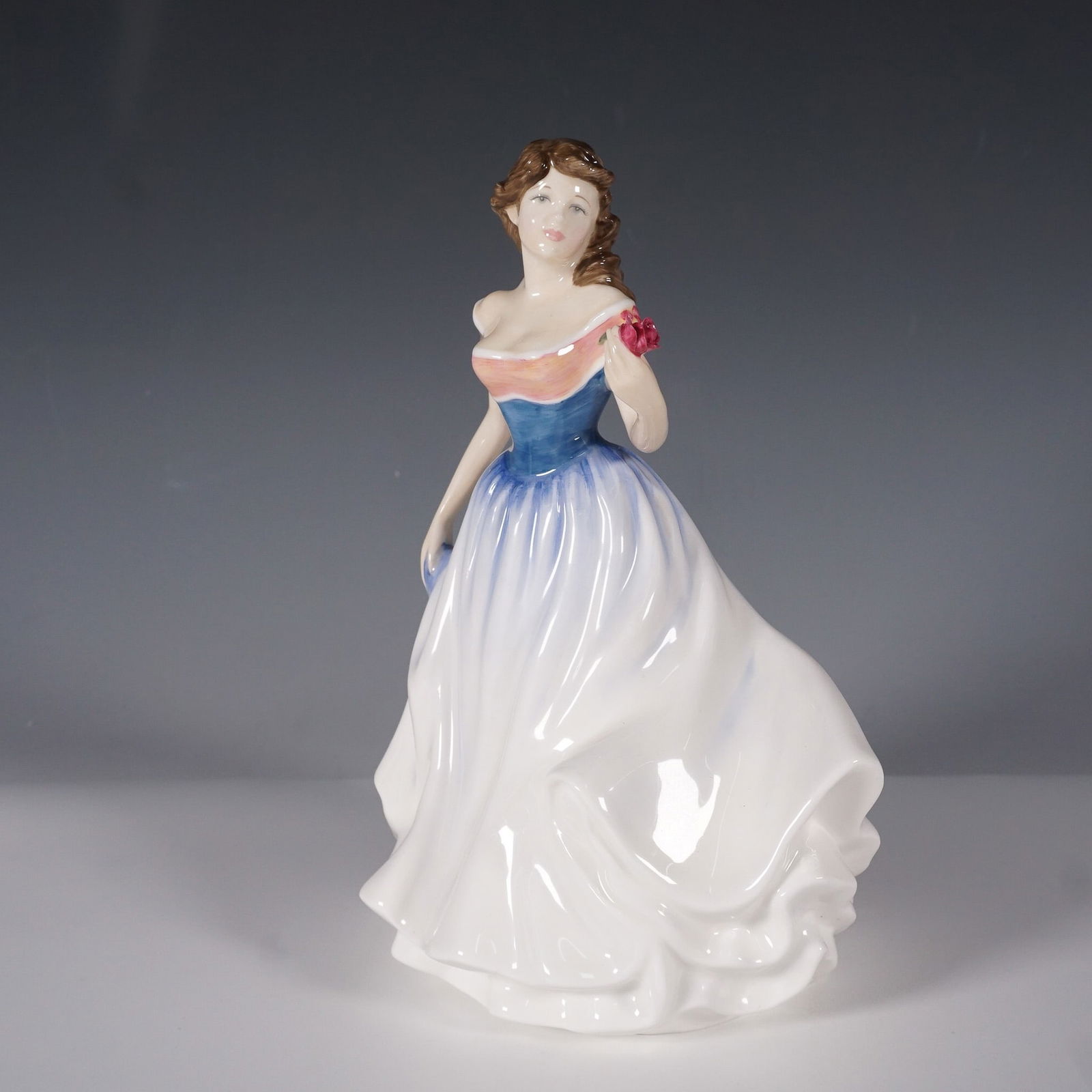 Royal Doulton Jayne HN4210 Figurine by Nada Pedley: A charming Royal Doulton figurine titled Jayne (HN4210), designed by Nada Pedley. This elegant porcelain figurine, released in 1999, portrays a graceful young woman in a flowing white gown with a blue