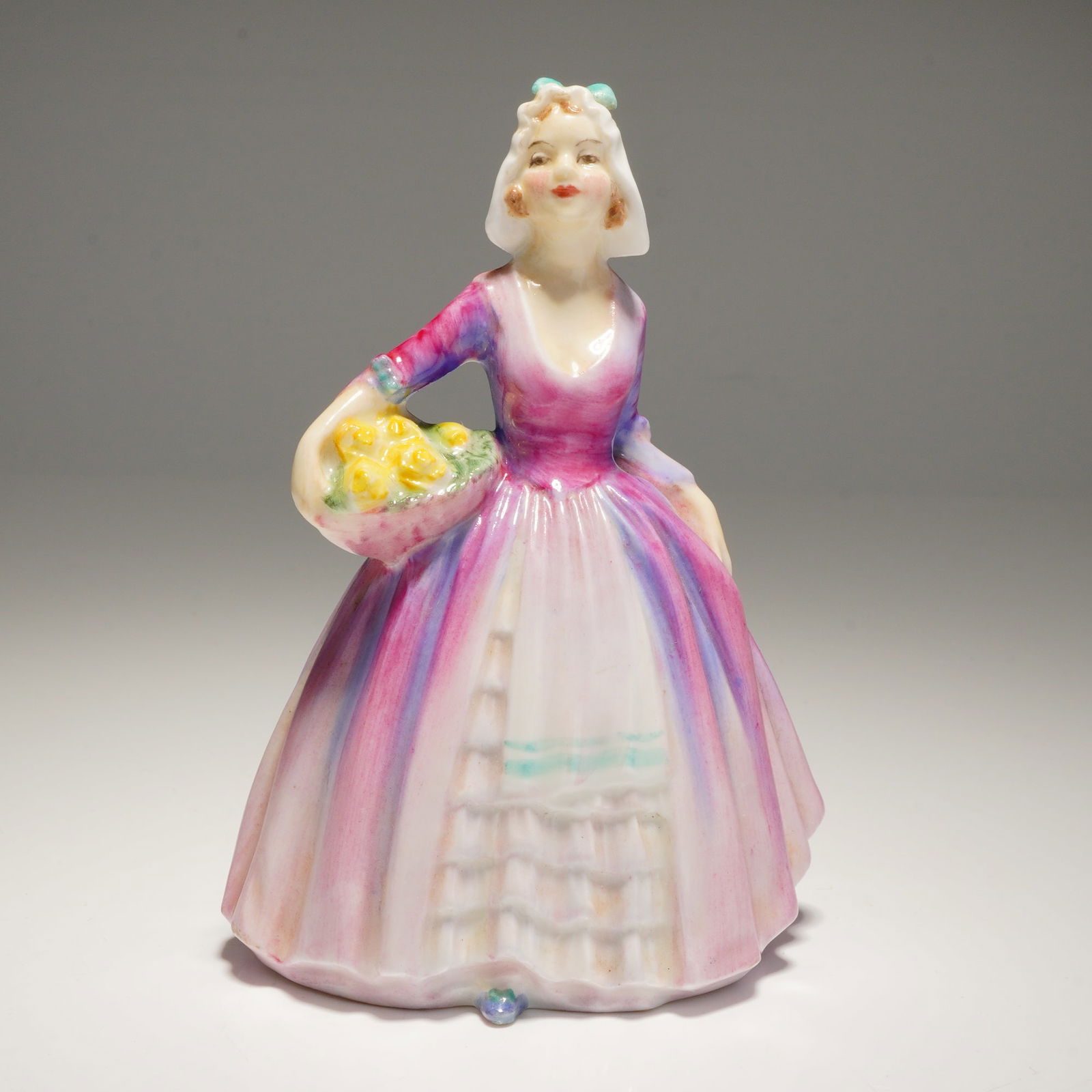 Royal Doulton Miniature Figurine Janet M75: A Royal Doulton porcelain figurine, Janet M75, depicting a woman in a pink, purple, and white dress holding a basket of yellow flowers, marked "BONE CHINA" and "RN.No. 778640." Dimensions: 3.00"L x 2.