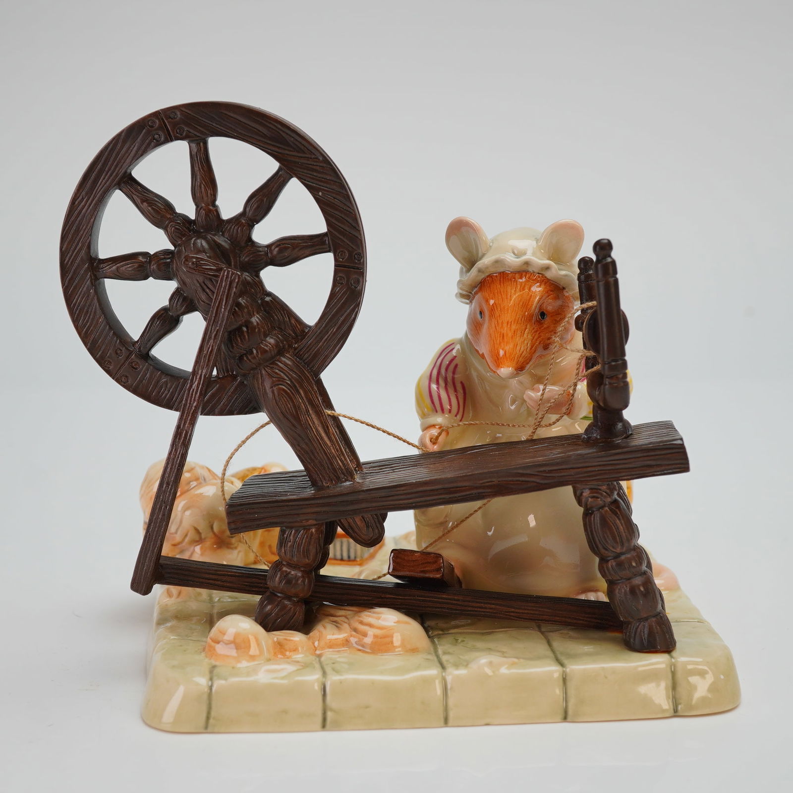 Royal Doulton Brambly Hedge Figurine, Lily Weaver Spinning DBH58: This Royal Doulton Brambly Hedge is a hand-decorated ceramic piece from the High Hills Collection. The figure depicts an anthropomorphic mouse in traditional country attire, including a bonnet and str