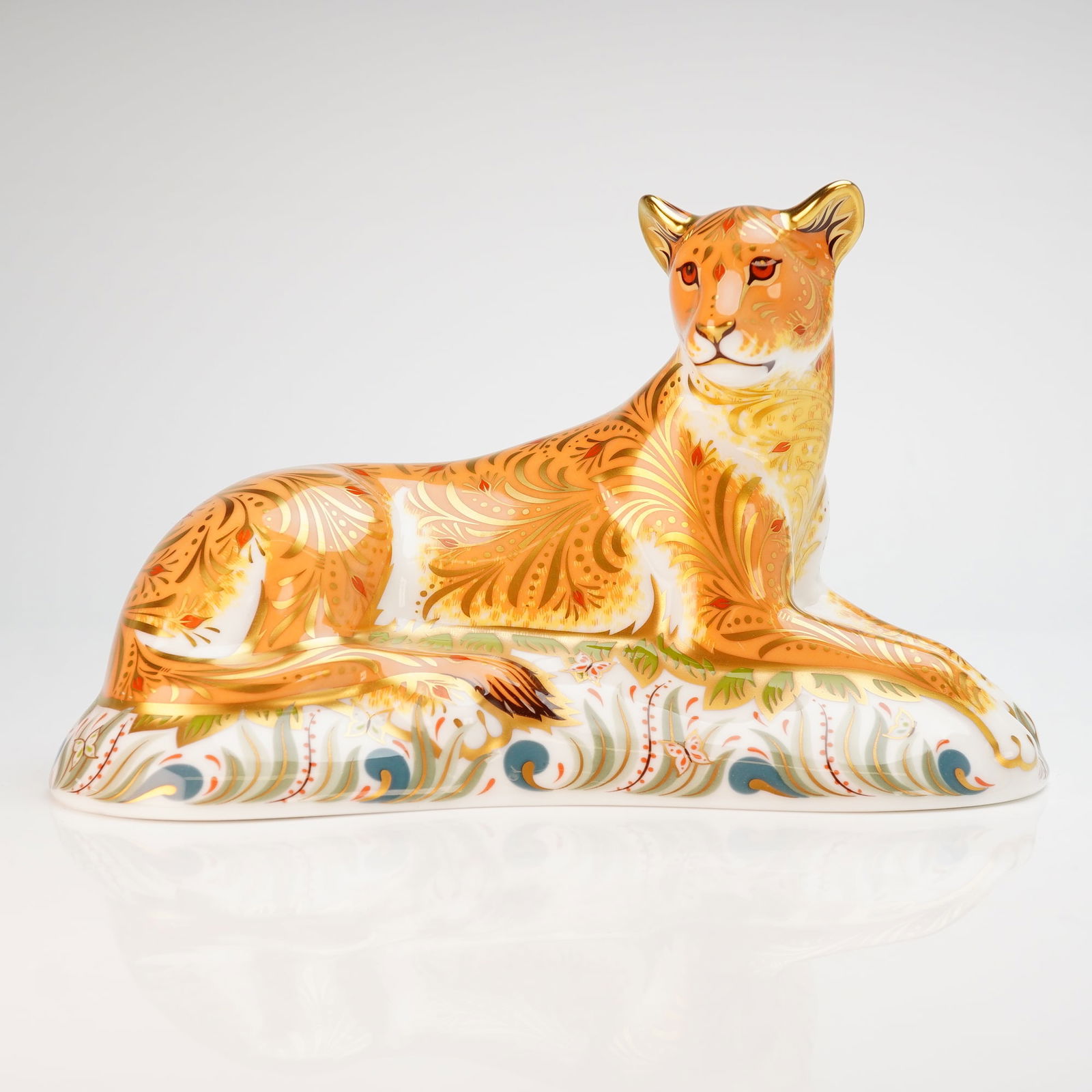 Royal Crown Derby Paperweight Lioness with Box: A Royal Crown Derby fine bone china paperweight titled Lioness. The figure is modeled in a recumbent pose and features stylized gilt scrollwork and foliate motifs over a russet and white ground. The