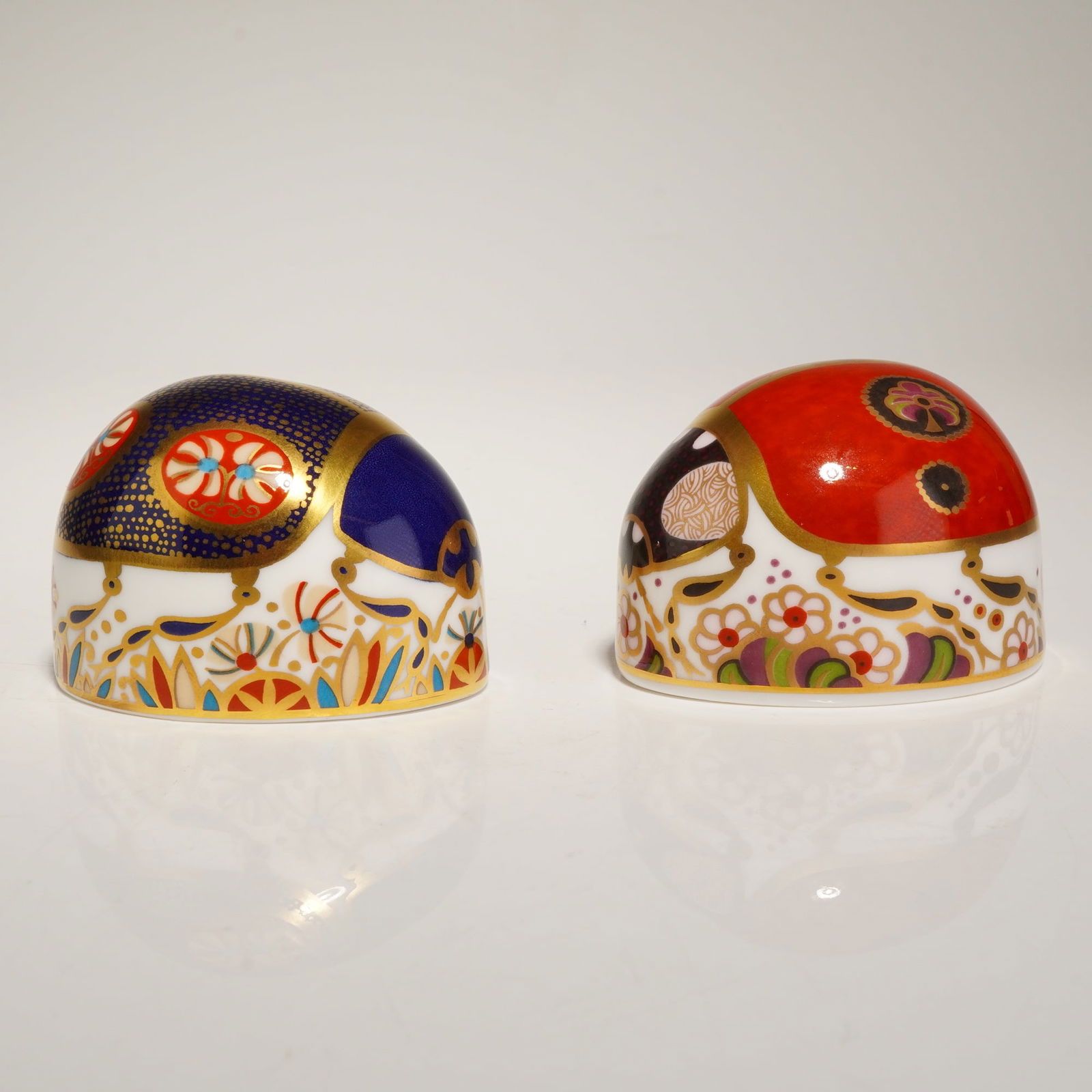 2pc Royal Crown Derby Imari Ladybird Paperweights: Royal Crown Derby bone china paperweights in the Imari pattern, modeled as ladybirds. The pieces are decorated in cobalt blue, iron red, and gold gilding over a white bone china body. The forms are
