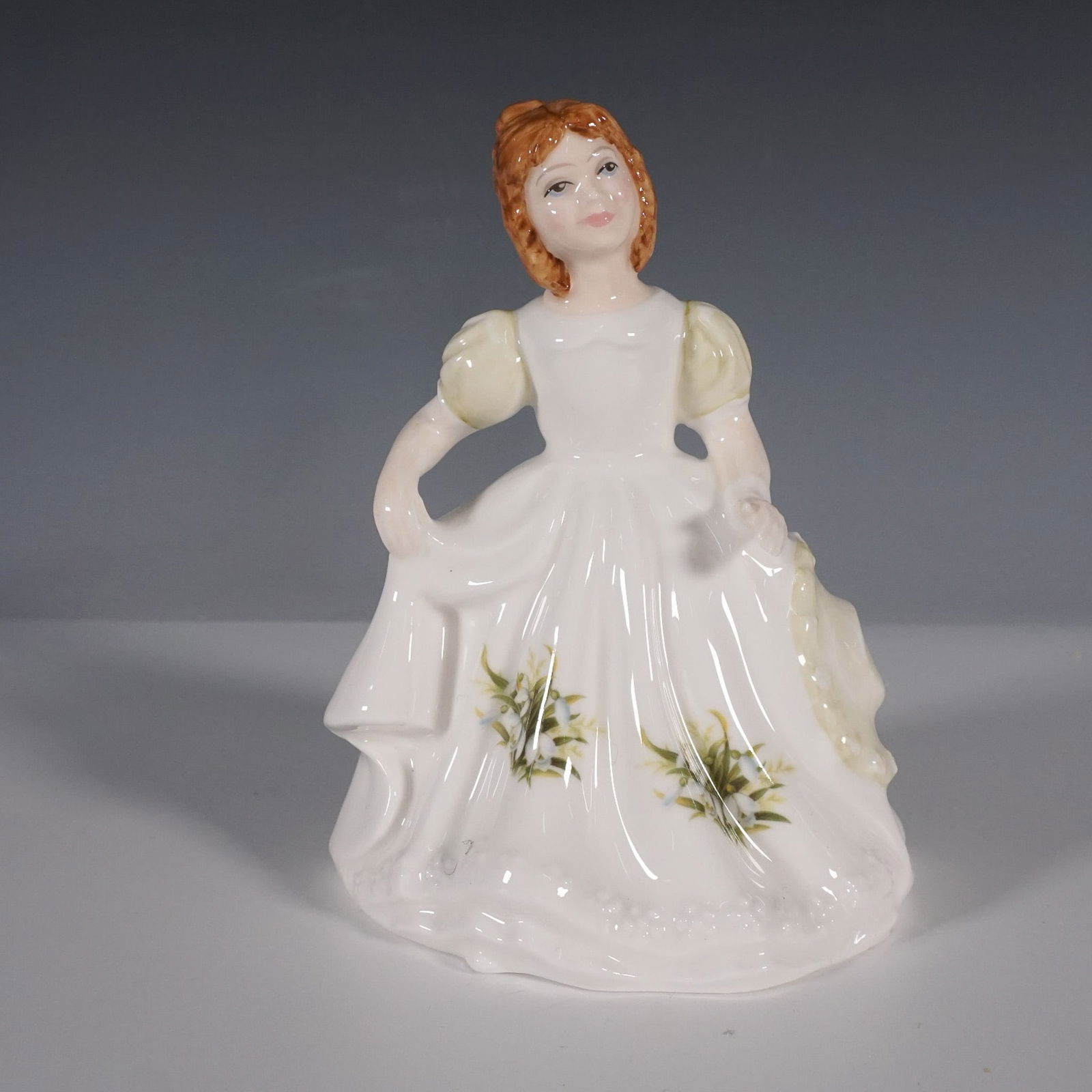 Royal Doulton Figure of the Month, January HN3330: This Royal Doulton porcelain figurine is part of the Figure of the Month series. This charming piece features a young girl in an elegant flowing dress adorned with delicate snowdrop flowers,