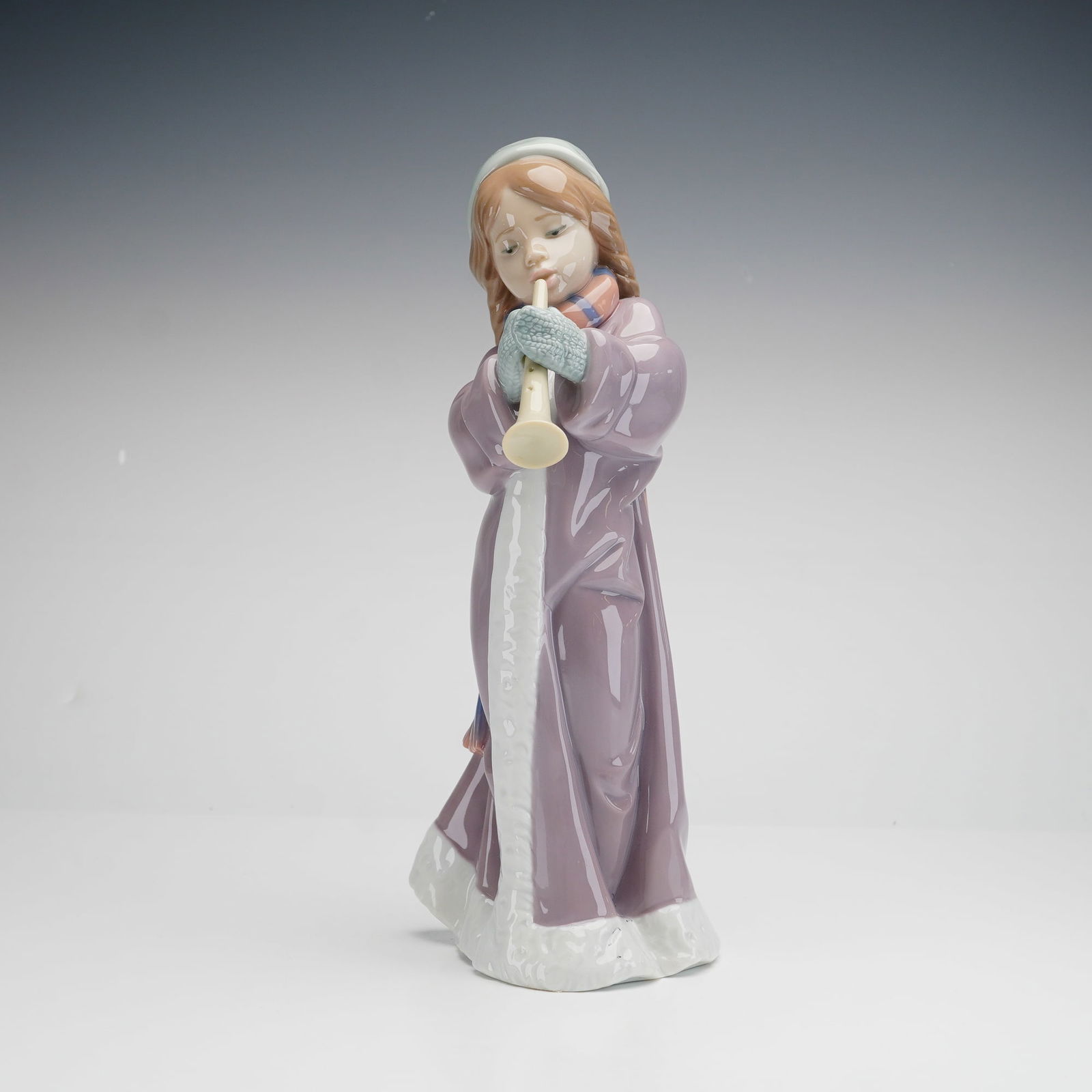 Lladro Porcelain Figurine, A Christmas Song 01006532: A Lladro glazed porcelain figurine depicting a young girl in winter attire playing a flute. The figure is modeled in a contemporary style, featuring a girl in a long purple coat with white trim, a str