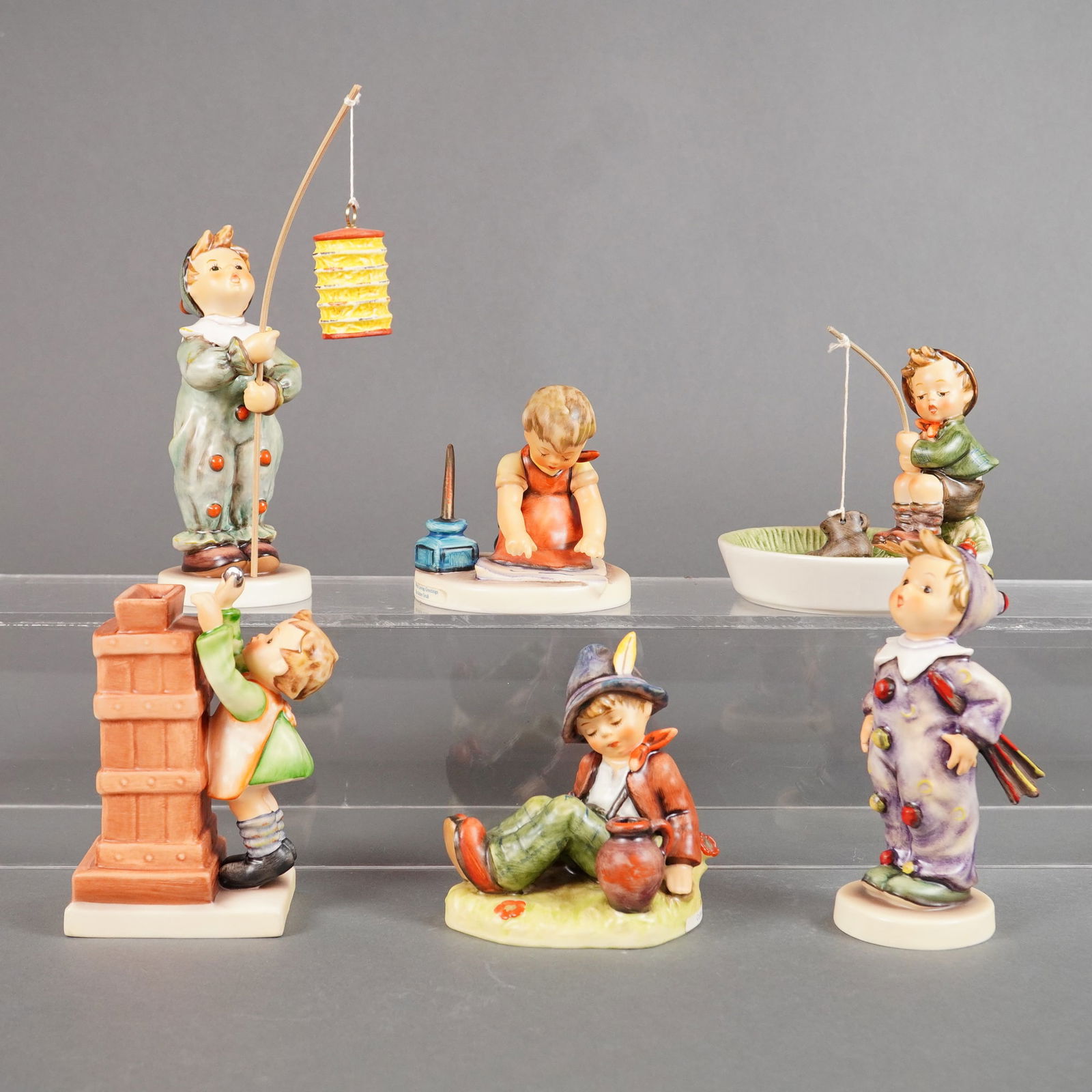 A Collection of Six Goebel Hummel Figurines Parade of Lights and More: A collection of six (6) hand-painted ceramic Goebel Hummel figurines, including pieces from the Parade of Lights series and other related scenes. The 6pc collection features children in various activi