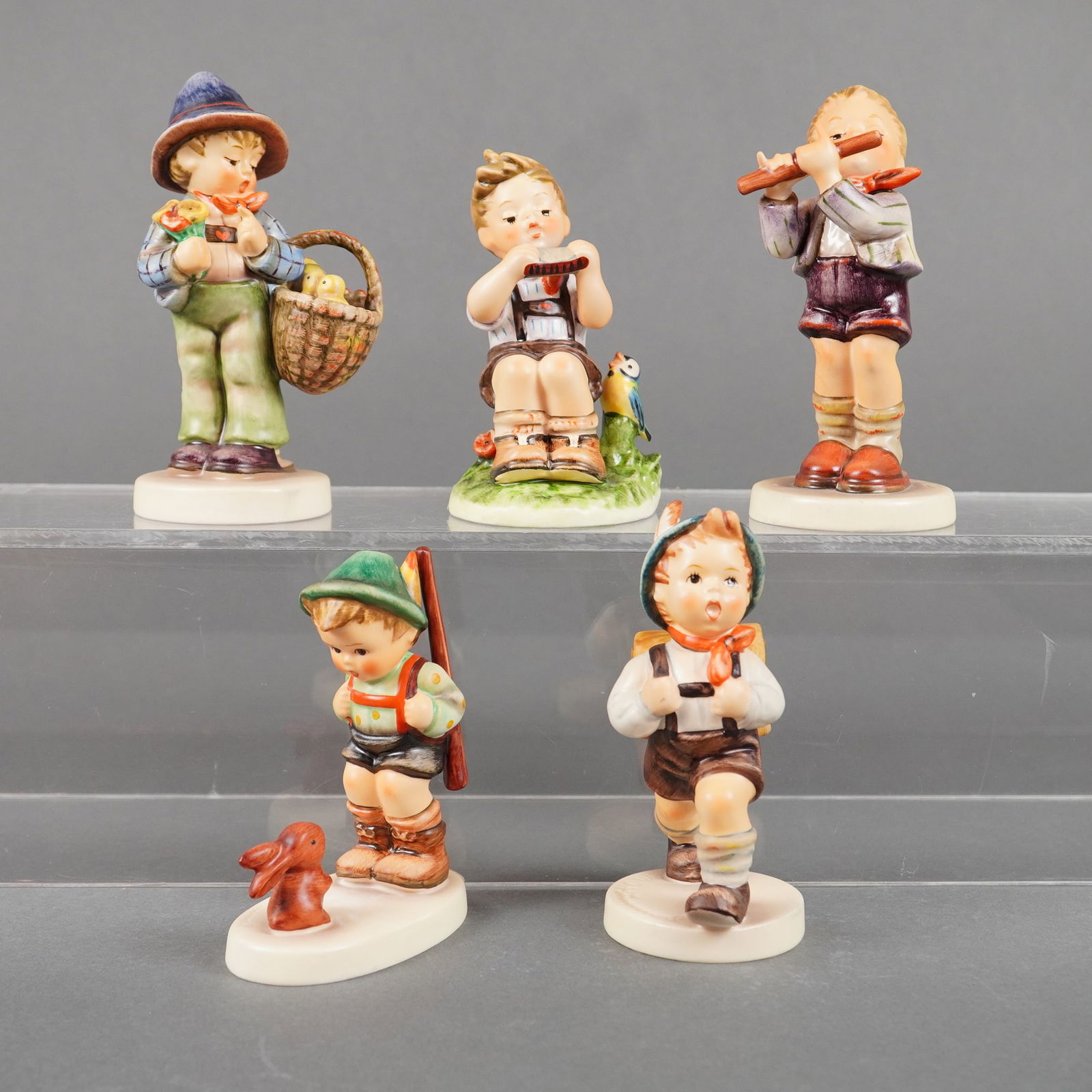 5 Goebel Hummel Figurines incl. Easter Greetings: A collection of five Goebel Hummel style porcelain figurines, executed in brightly colored hand-painted glazes. The collection depicts young boys in traditional Germanic or Bavarian folk attire engage