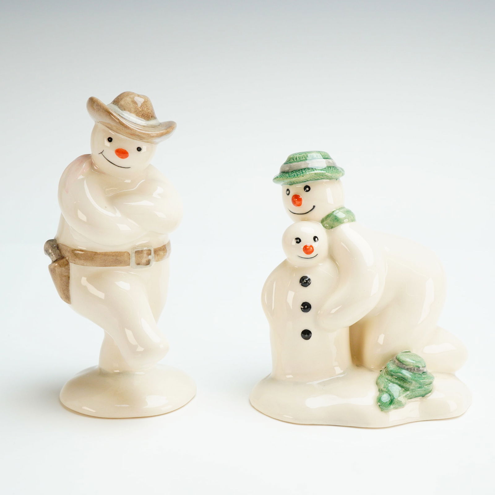 Two Royal Doulton Snowman Figurines, DS 26 and DS 6: Two Royal Doulton inspired by the Raymond Briggs series. These items are constructed of glazed ceramic with a high-gloss cream finish and hand-painted accents. The collection includes Cowboy Snowman (