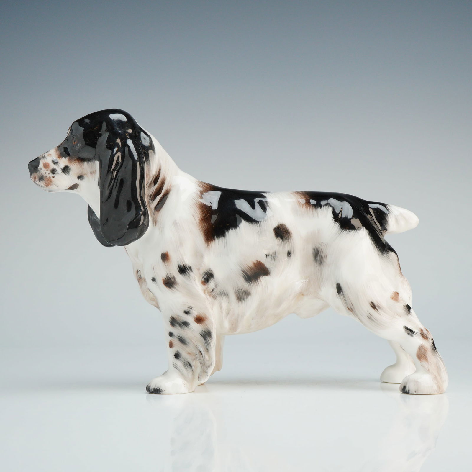 Royal Doulton Bone China Figurine, Cocker Spaniel HN1109: Depicting a tricolor Cocker Spaniel in a standing pose. The piece features a high-gloss glazed finish with black and tan markings on a white ground. The dog is modeled with characteristic long, pendul