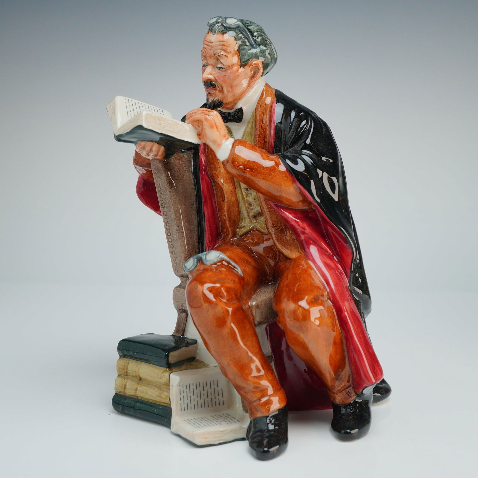 Royal Doulton Figurine Professor HN2281: A Royal Doulton porcelain figurine designed by M. Nicoll. This polychrome glazed figure depicts a seated male academic with grey hair, a goatee, and spectacles resting on his forehead. The figure is d