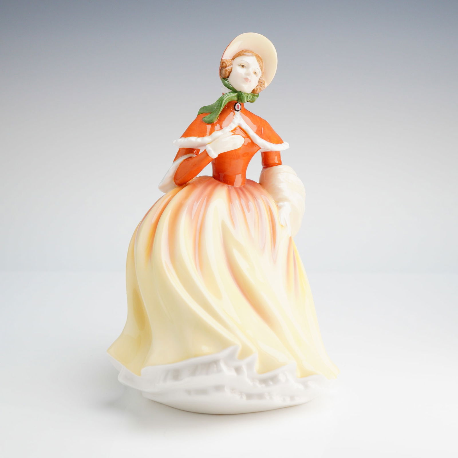 Royal Doulton Pretty Ladies Figurine, Autumn HN 5323: A single Royal Doulton figurine, depicting a woman in an orange jacket and voluminous yellow and orange skirt. Royal Doulton backstamp on base. Dimensions5.50"L x 8.25"H Weight1.00 lb