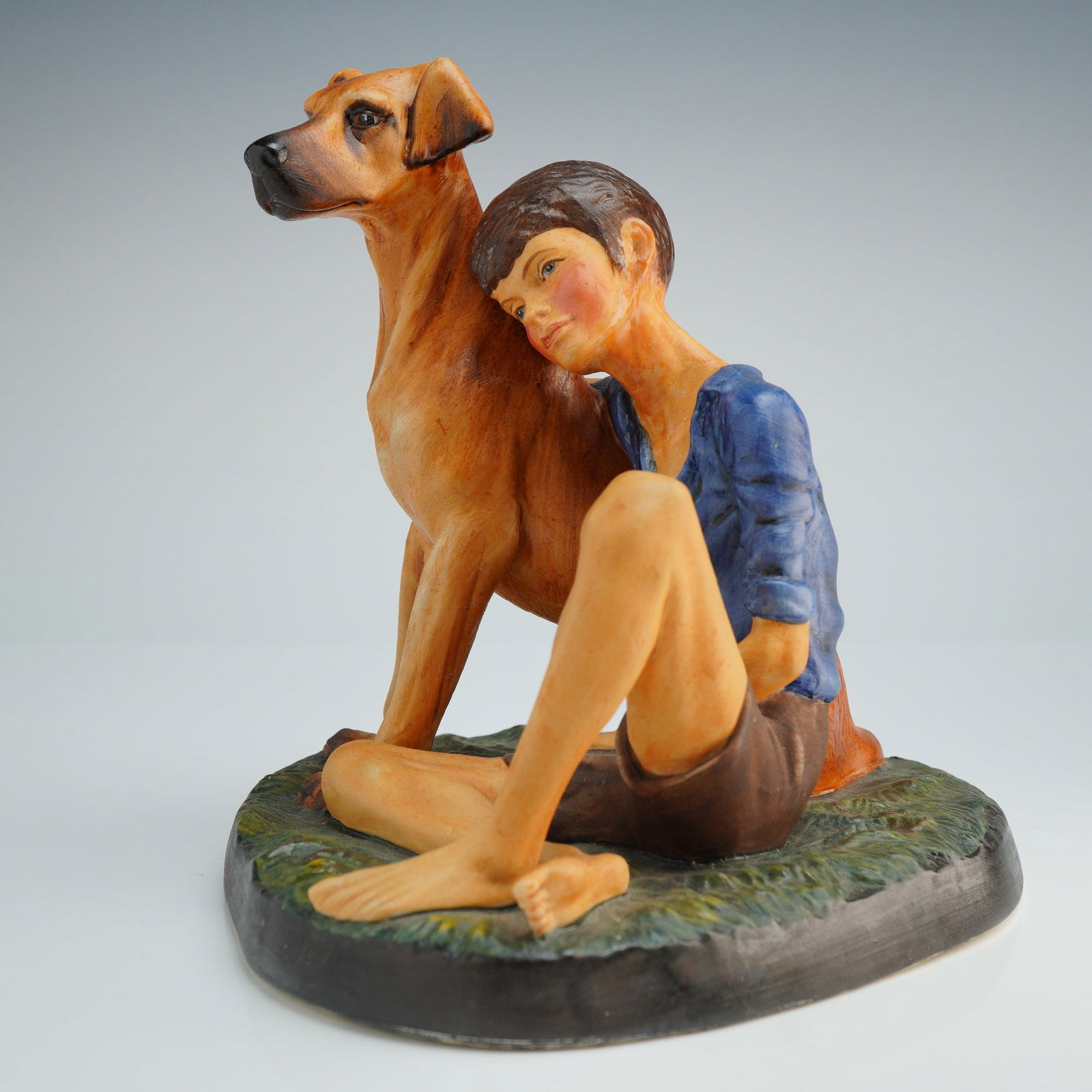 Royal Doulton Figurine Buddies HN2546: This Royal Doulton figurine features a matte finish and dates to circa 1972. The porcelain piece depicts a young boy wearing a blue short-sleeved shirt and brown shorts seated on a textured green base