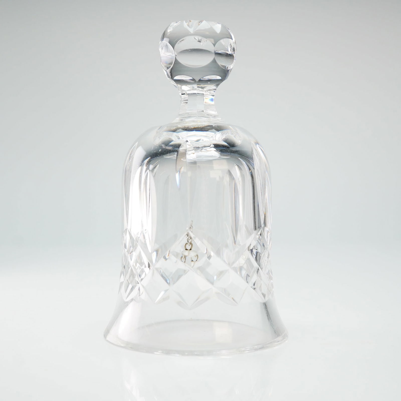 Waterford Crystal Table Bell, Lismore: The piece is crafted from clear lead crystal and features a faceted globular handle above a bell-shaped body. The decoration consists of vertical wedge cuts above a band of cross-hatched diamond cuts.