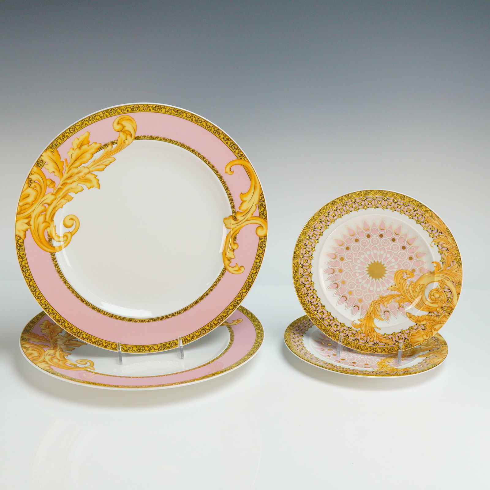 Rosenthal Versace Porcelain Four Plate Set, Les Reves Byzantins: This collection features a pink, white, and gold color palette with Baroque-inspired ornamentation. The design includes acanthus leaf scrollwork, geometric borders, and a central sunburst motif on the