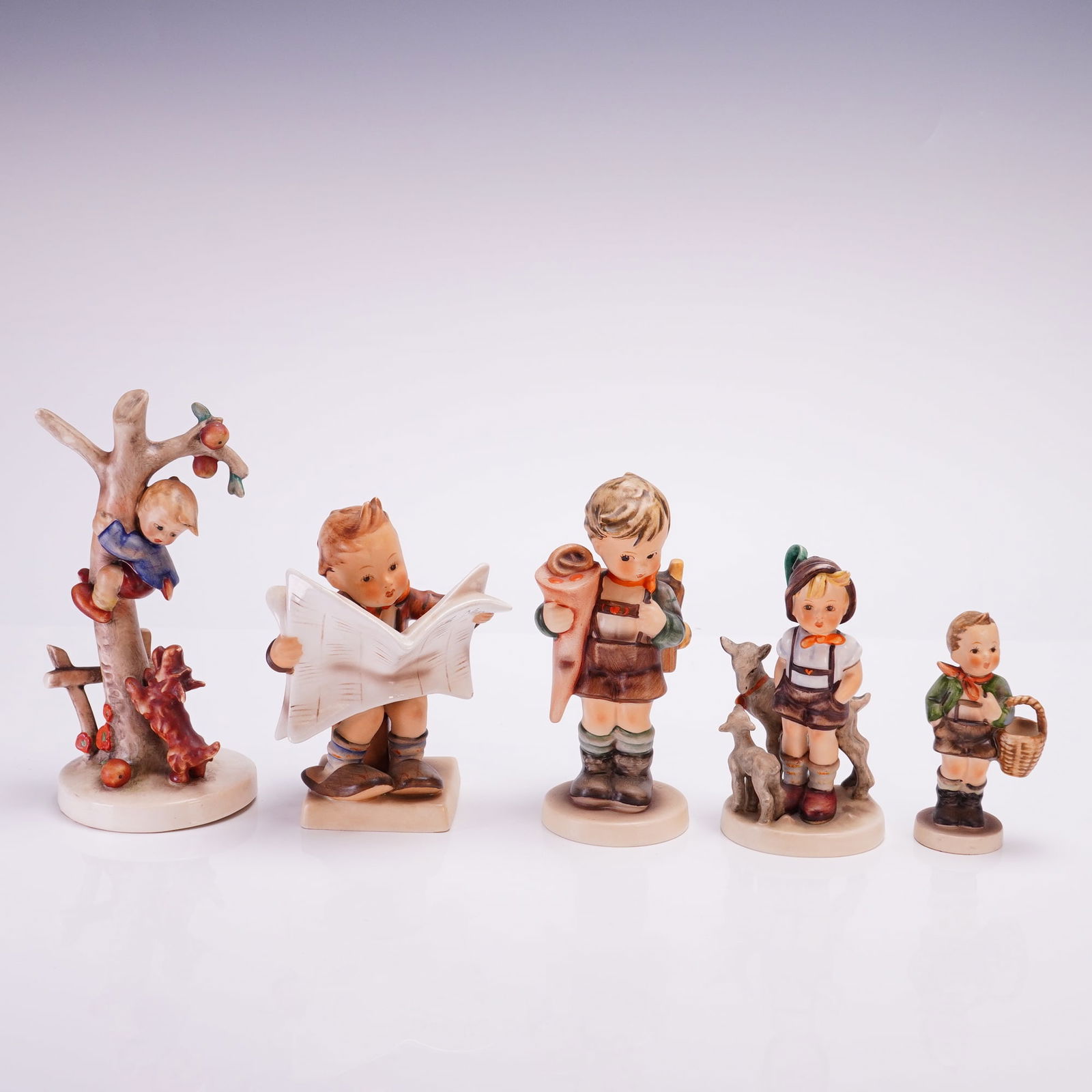 5pc Collection of Goebel Hummel Porcelain Figurines: Figurines depicting children in various thematic scenes. The group includes a boy in a fruit tree with a dog, a seated boy reading a newspaper titled Latest News, a schoolboy carrying a school cone an