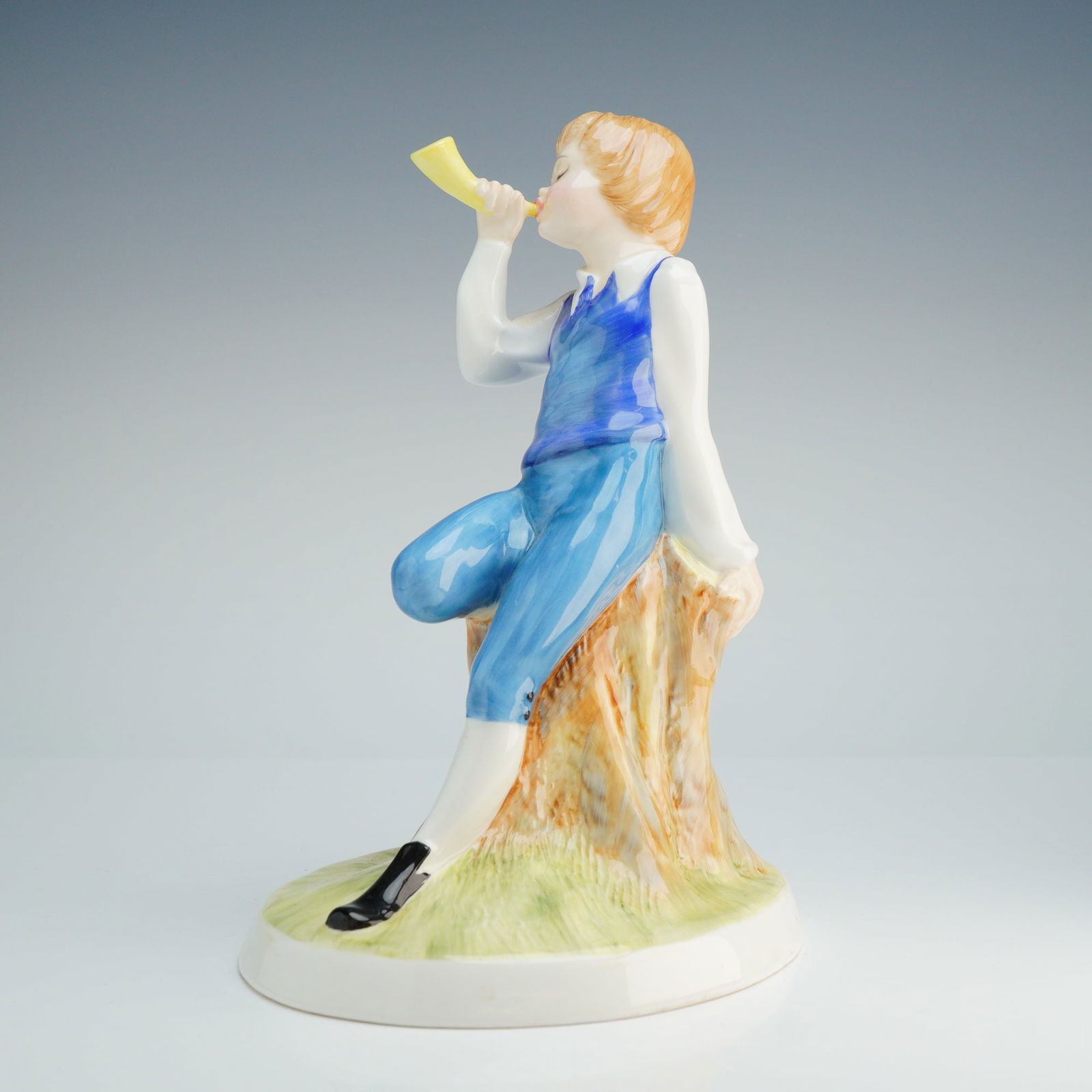 Royal Doulton Nursery Rhymes Figurine, Little Boy Blue HN3035: This hand-made and hand-decorated piece was modeled by Adrian Hughes. The figurine depicts a young boy with light brown hair wearing a blue vest and trousers over a white shirt, seated on a naturalist