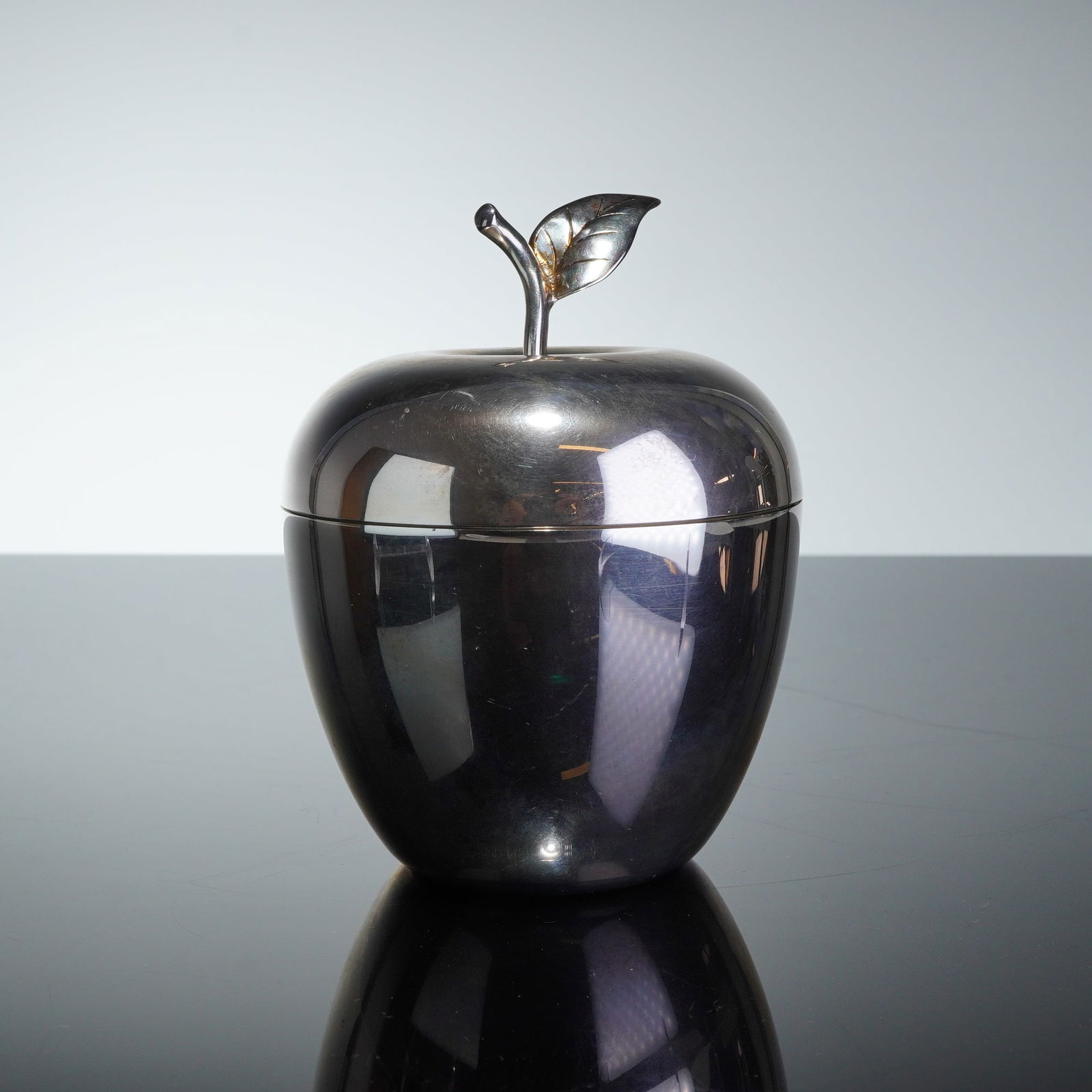 Tiffany & Co. Sterling Silver Apple-Form Trinket Box: A Tiffany & Co. sterling silver trinket box designed in the realistic form of an apple. The piece consists of a deep circular base and a removable lid topped with a cast stem and single-leaf handle. T