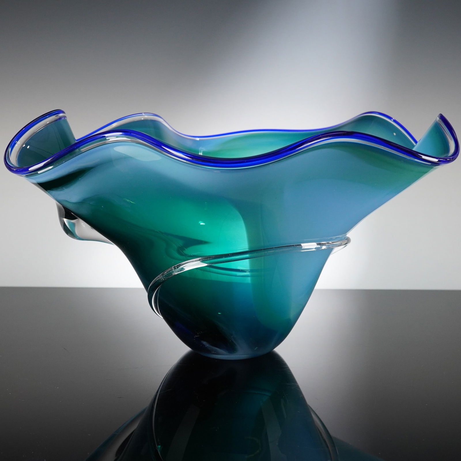 Susan Anne Free Form Blue Art Glass Bowl: A single studio art glass vessel from Susan Anne, designed in a free form, asymmetrical bowl shape. The piece is executed in blown glass with a layered construction, transitioning in color from opaque