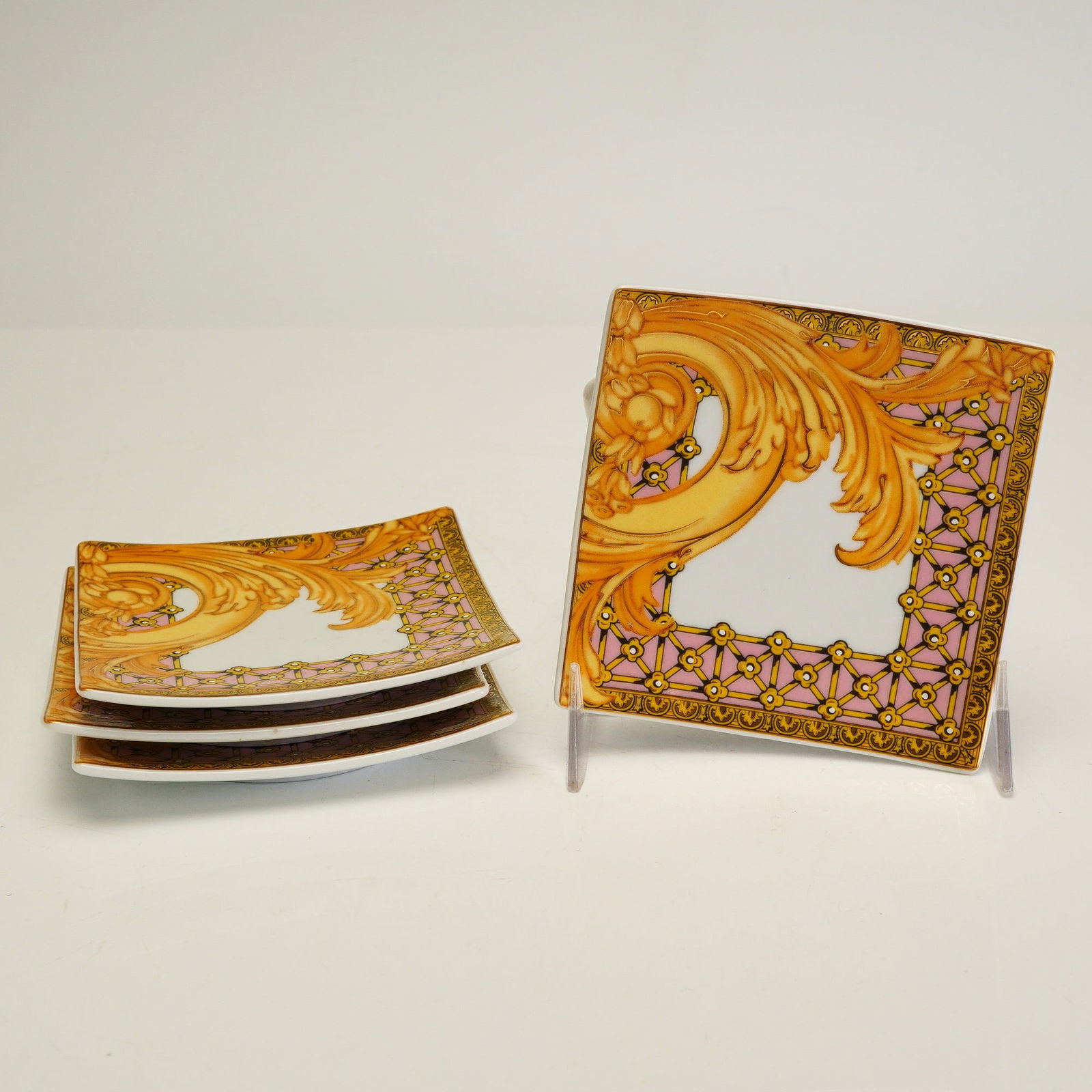 4pc Versace Rosenthal Porcelain Small Square Dishes, Les Reves Byzantins: Each dish features a Neo-Baroque design with golden acanthus leaf scrollwork and a pink border accented by gold-tone latticework and floral patterns surrounding a central white square. The underside o