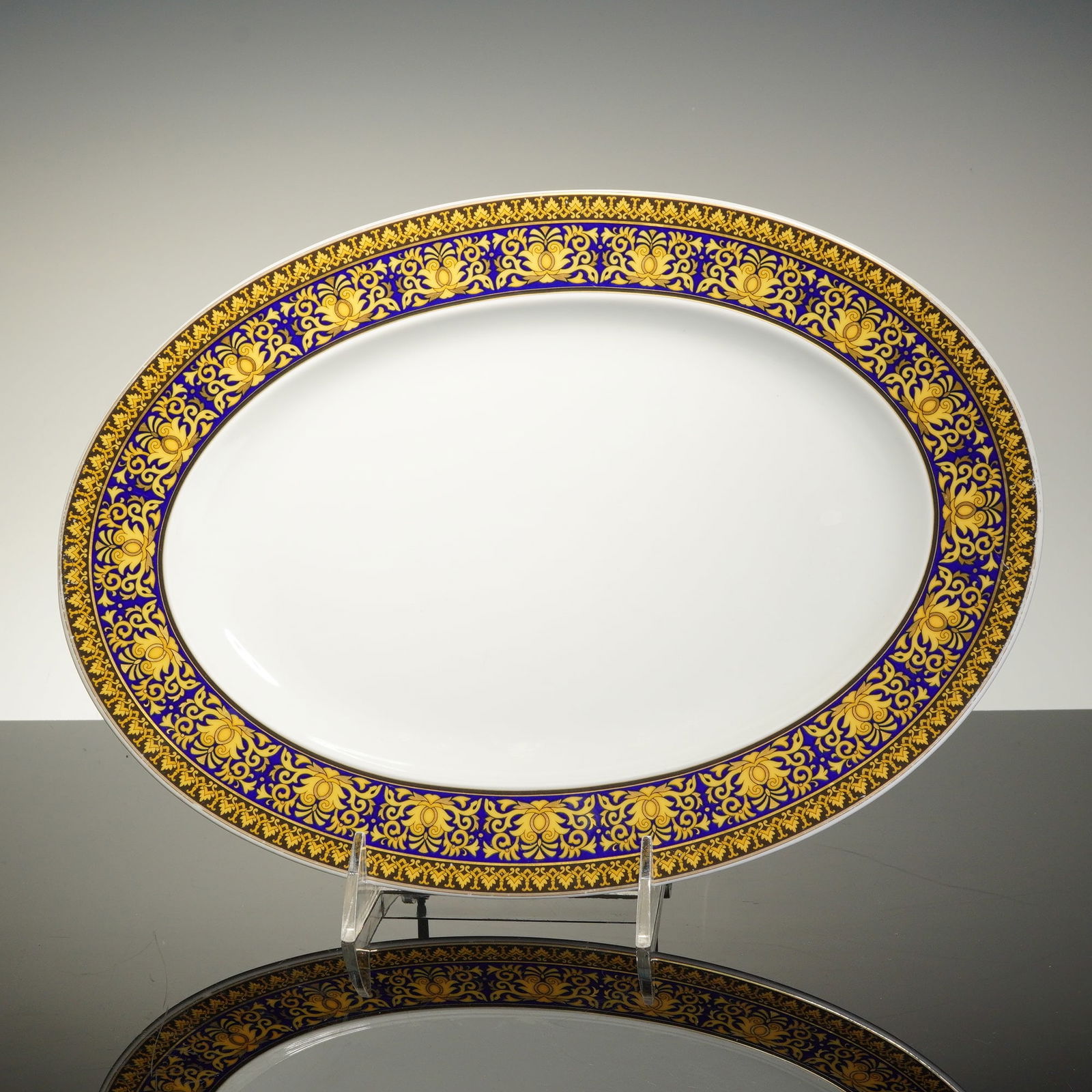 Rosenthal Versace Porcelain Oval Platter, Medusa Blue: This Rosenthal Versace Medusa Blue platter is composed of white glazed porcelain. The oval form features a wide rim decorated with a cobalt blue band overlaid with gold-toned scrolling foliate and flo