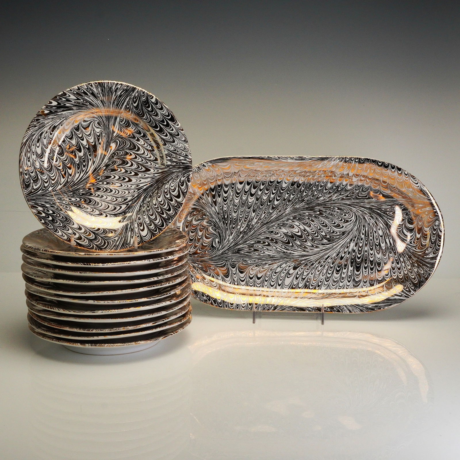 13pc Juliska Firenze Serving Dish and Cocktail Plates, Medici Gold-Platinum: A collection of twelve circular cocktail plates and one oval serving dish. The pieces are decorated with an intricate feathered marbling pattern in black, white, and metallic gold and platinum hues un