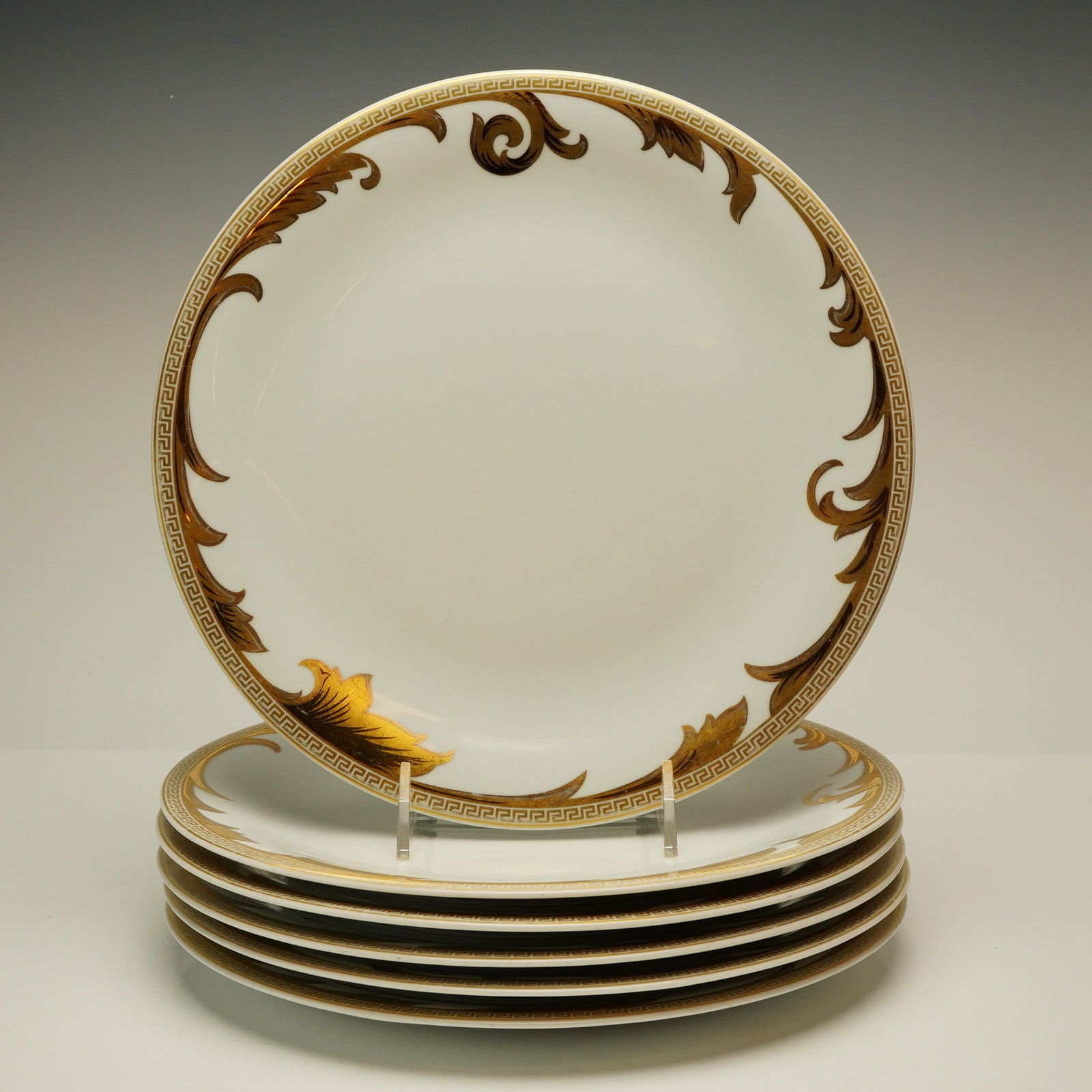 6pc Versace Rosenthal Dinner Plate Set, Arabesque Gold: Each plate is decorated with a gold-tone Greek key border and acanthus leaf scrollwork over a white ground. The undersides bear a black and gold circular maker's mark featuring the Rosenthal name and