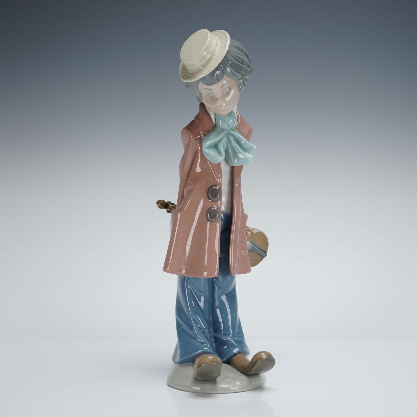 Lladro Clown with Violin Figurine 1005057: The figure, characterized as a melancholy clown or street musician, wears a cream straw hat, a long mauve overcoat, a teal bow tie, and blue trousers. He holds a violin concealed behind his back. The