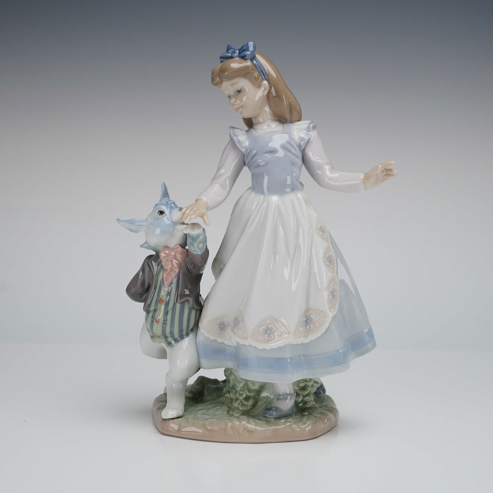 Lladro Porcelain Alice in Wonderland 1005740: A glazed porcelain figural group by Lladro, titled "Alice in Wonderland" (Model 5740). The piece depicts a young girl, identified as Alice, holding hands with an anthropomorphic White Rabbit figure dr