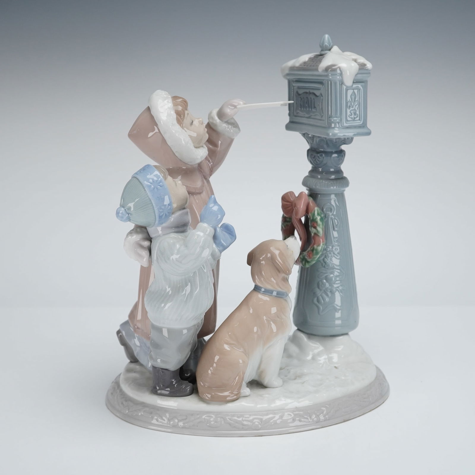 Lladro Winter Scene Figurine 1008010: The highly-glazed porcelain figurine depicts a winter holiday scene featuring two children, one taller and one shorter, dressed in pastel winter coats and hats (dusty rose and light blue). The taller